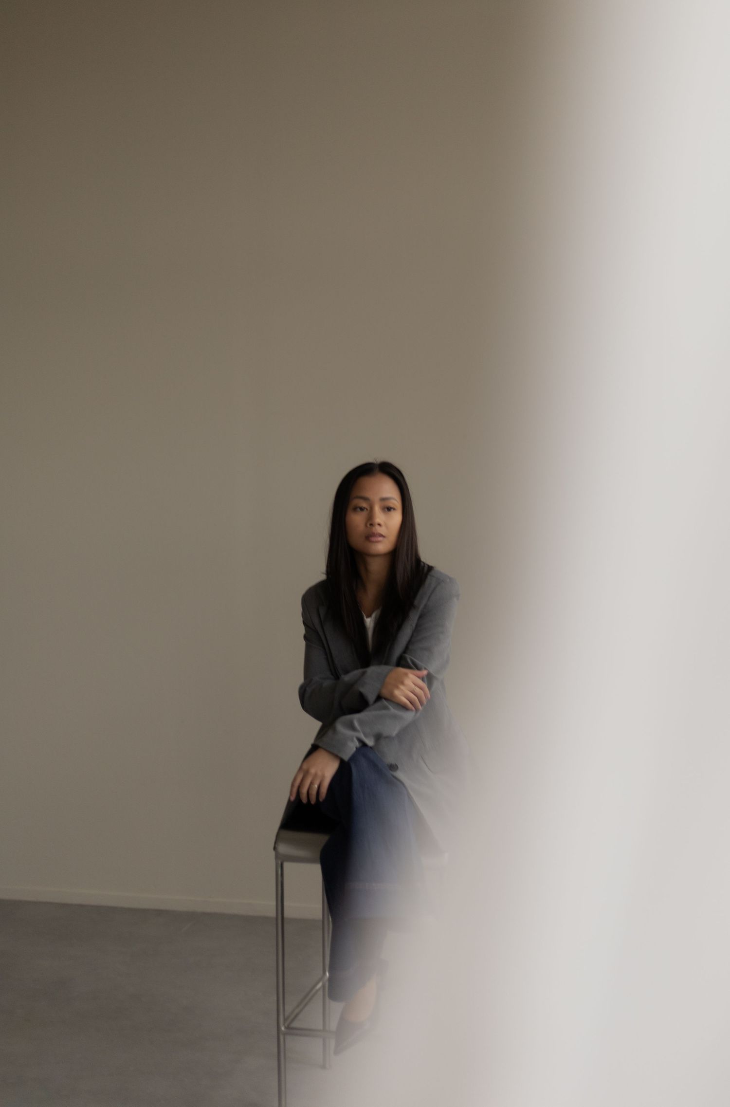 Artistic fashion poses with a chair against a minimalist grey backdrop.