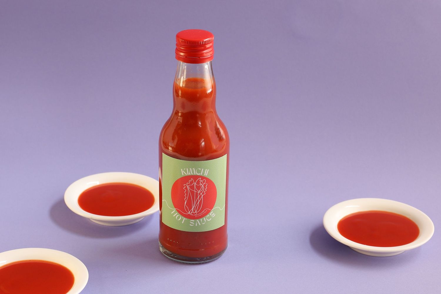 Hot sauce bottle and small dish photographed on purple background.