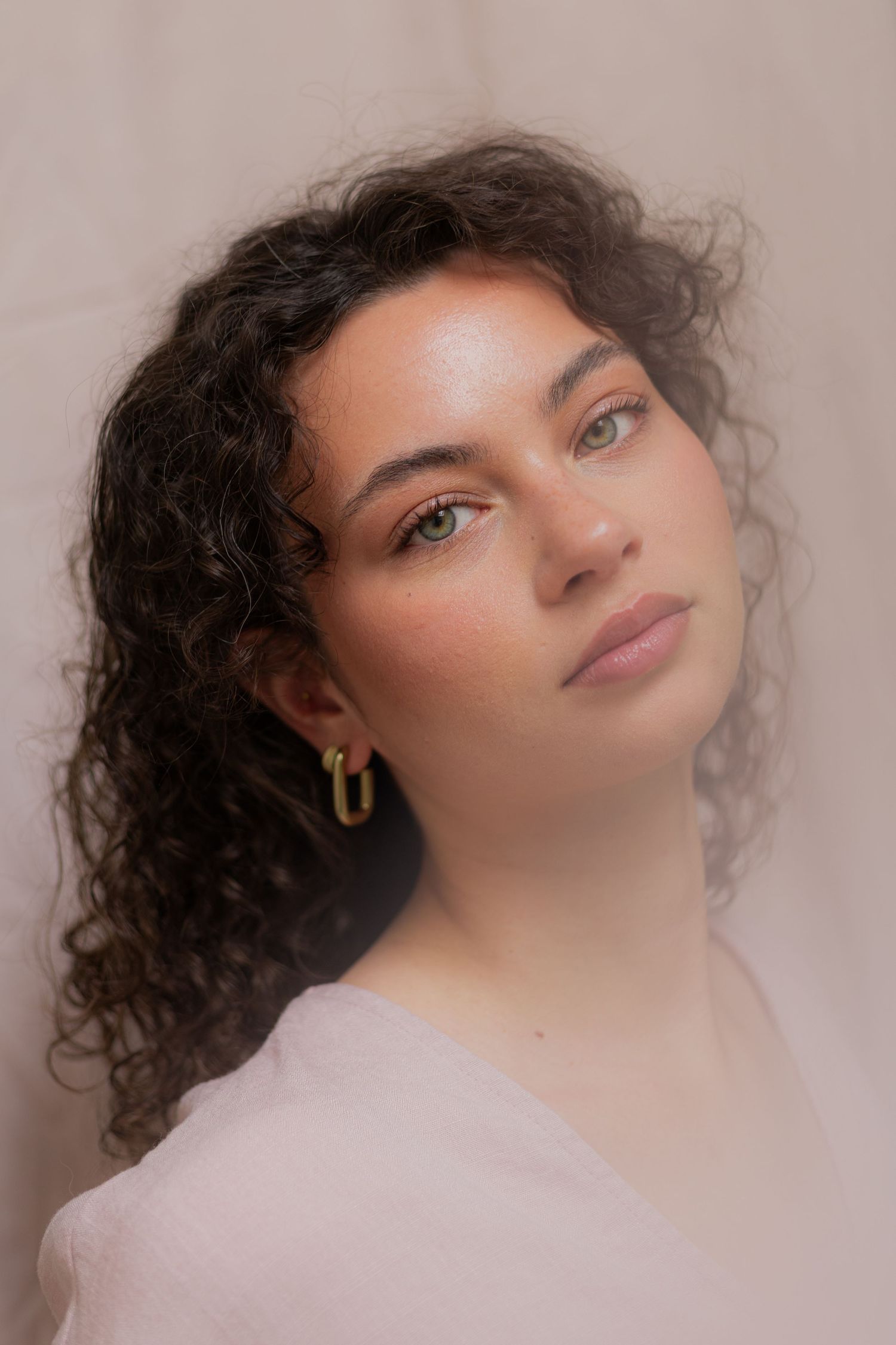 Artistic beauty portrait with soft pink background and dramatic lighting highlighting curly hair.