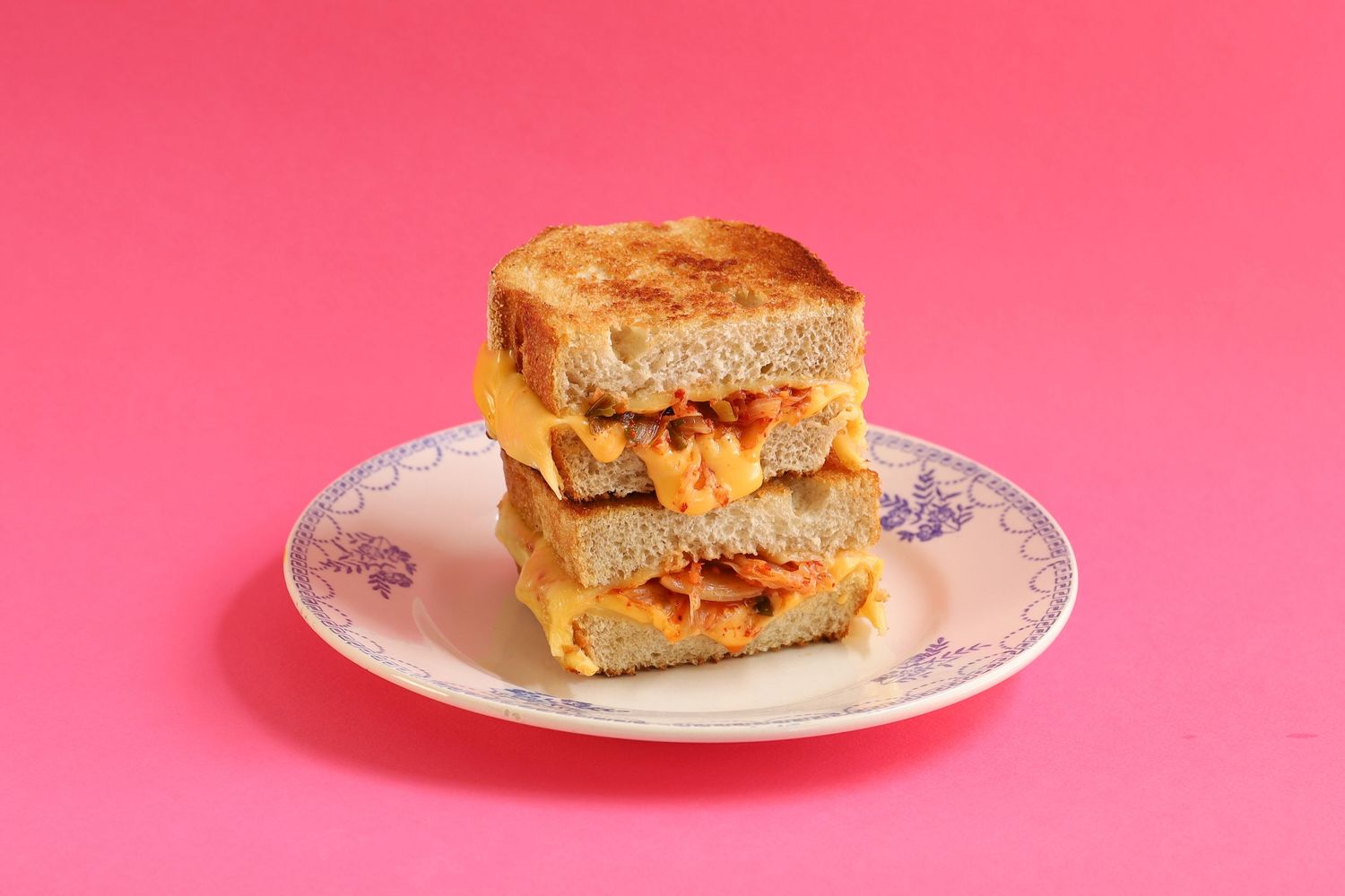 Grilled cheese sandwich halves on decorative plates against pink background.