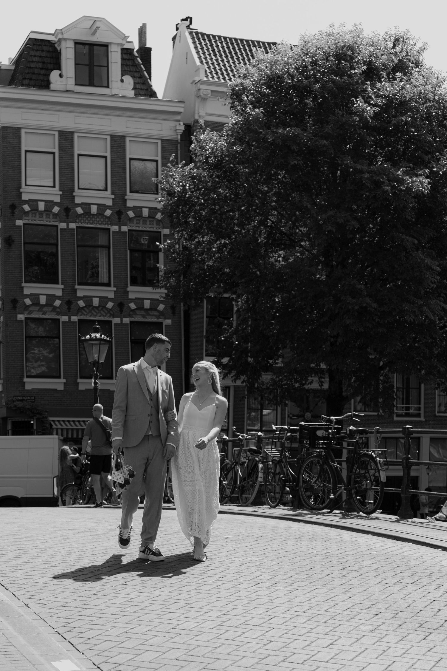 Two people walking on a cobblestone street in a historic Dutch neighborhood with traditional architecture.