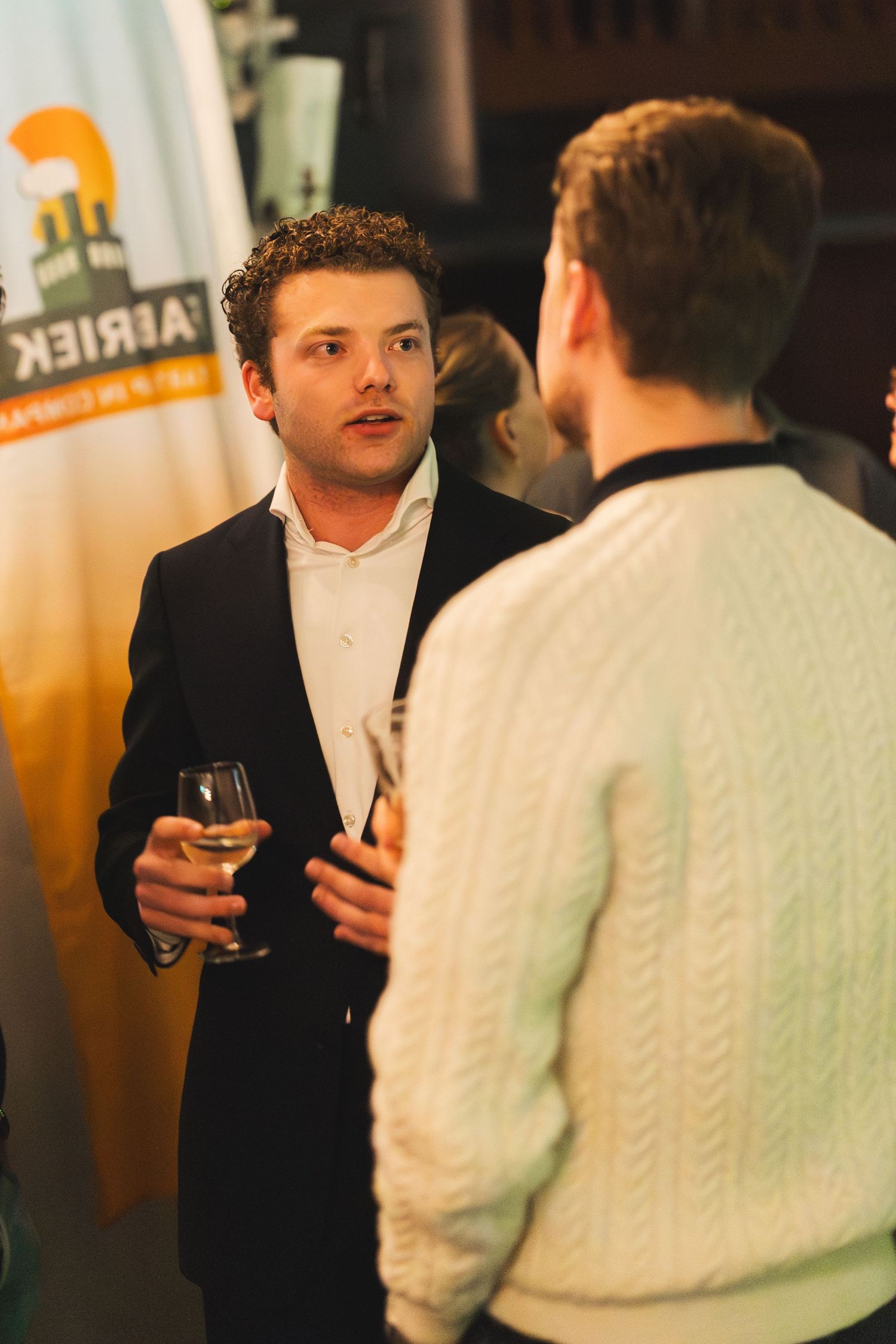 People in formal attire having drinks and conversation at an indoor social gathering.