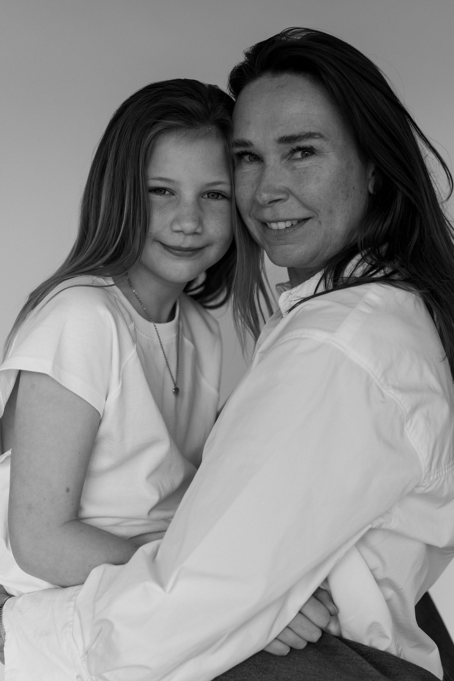 Black and white portrait of a smiling woman and young girl in white shirts posing closely together.