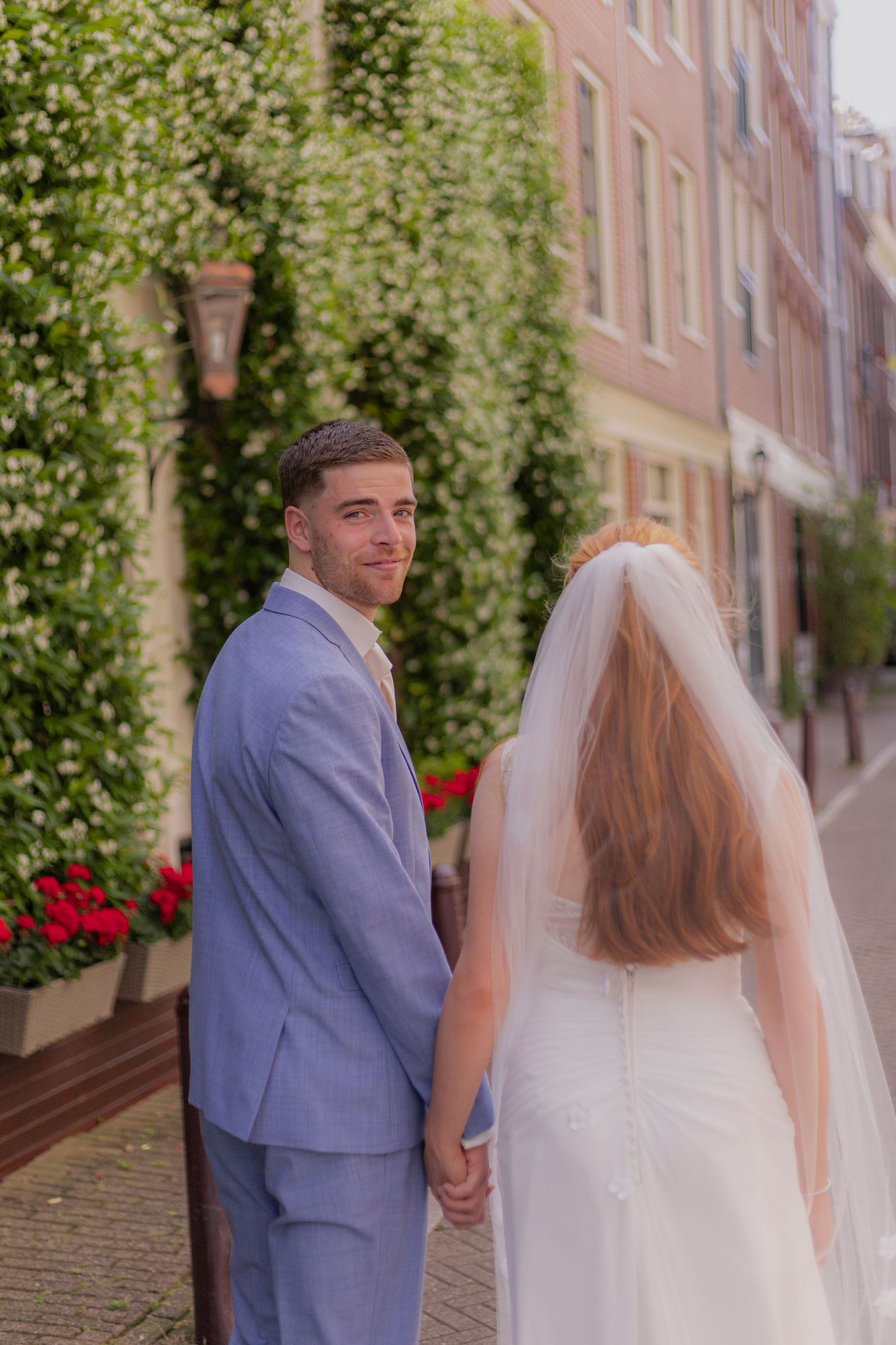 Newlyweds walk together on a charming European street lined with brick buildings and greenery.