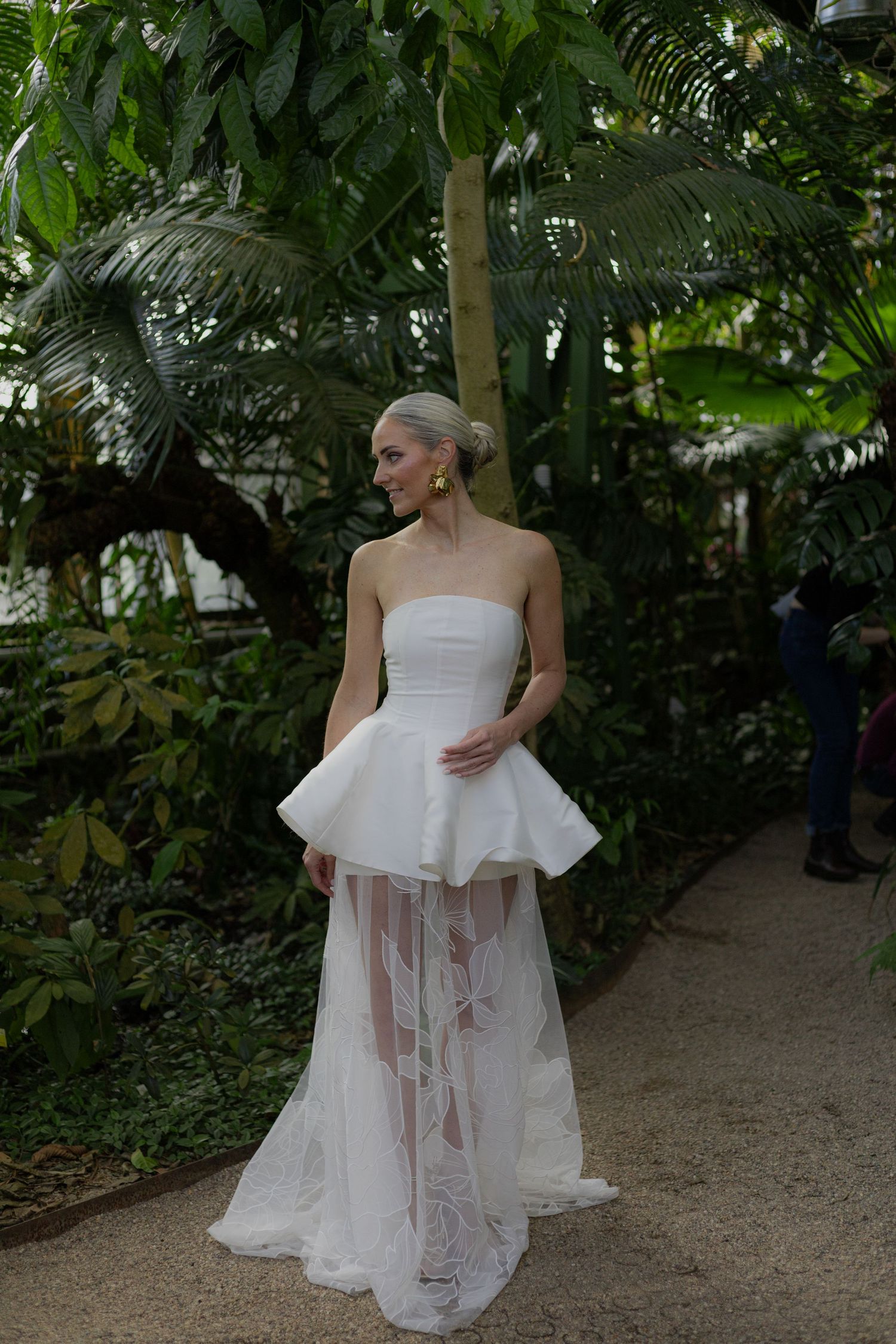 Modern wedding dress with structured peplum detail and sheer skirt photographed in a garden.