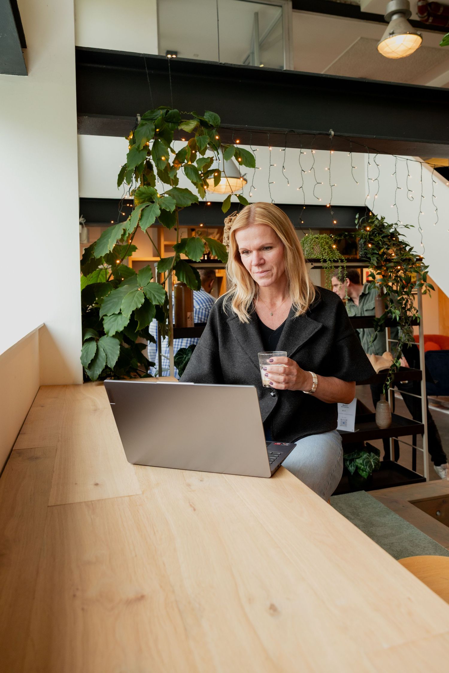 Person working at wooden desk in modern office space with plants and natural lighting.