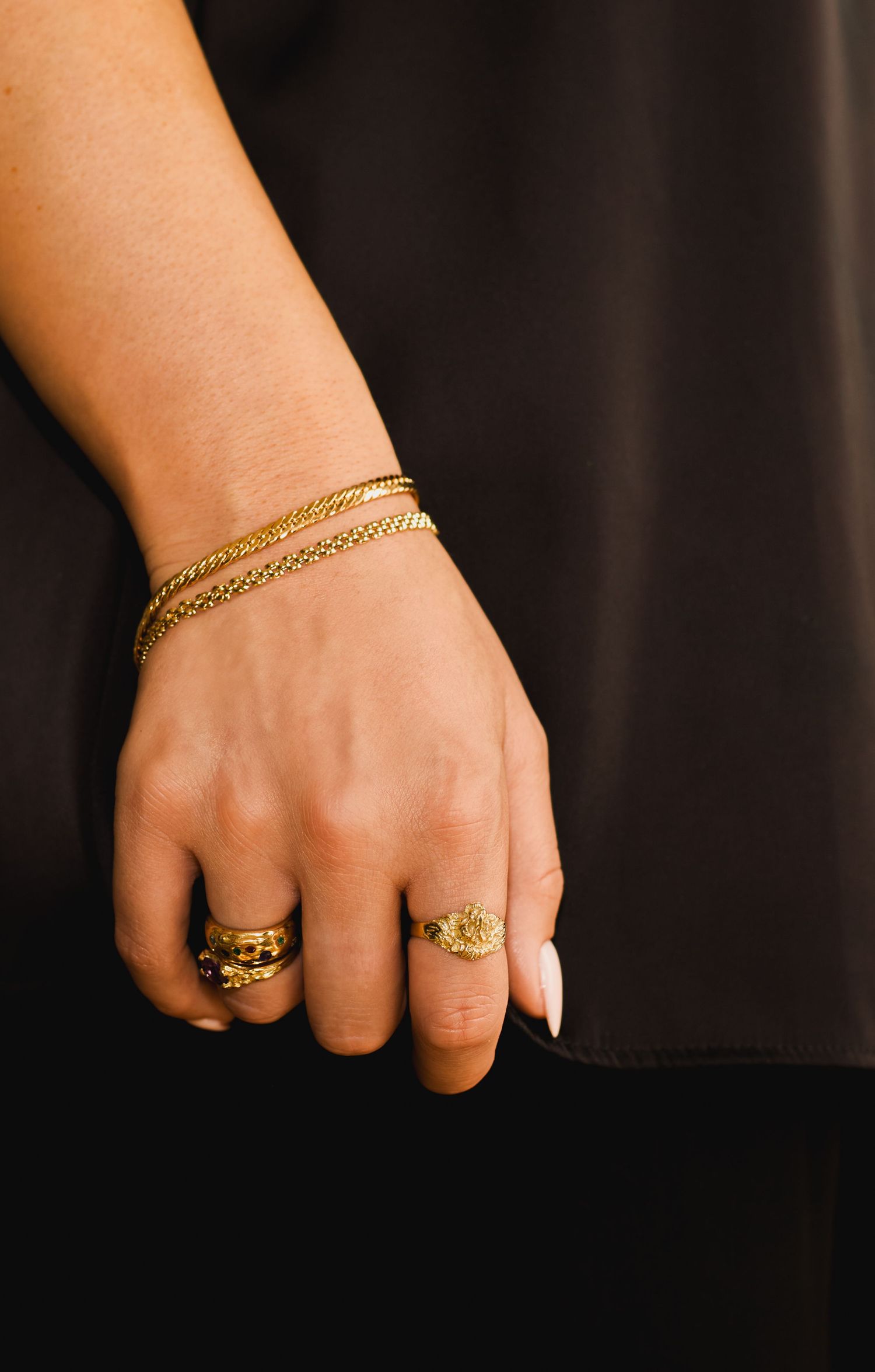 Hand adorned with gold jewelry including rings and a delicate chain bracelet.