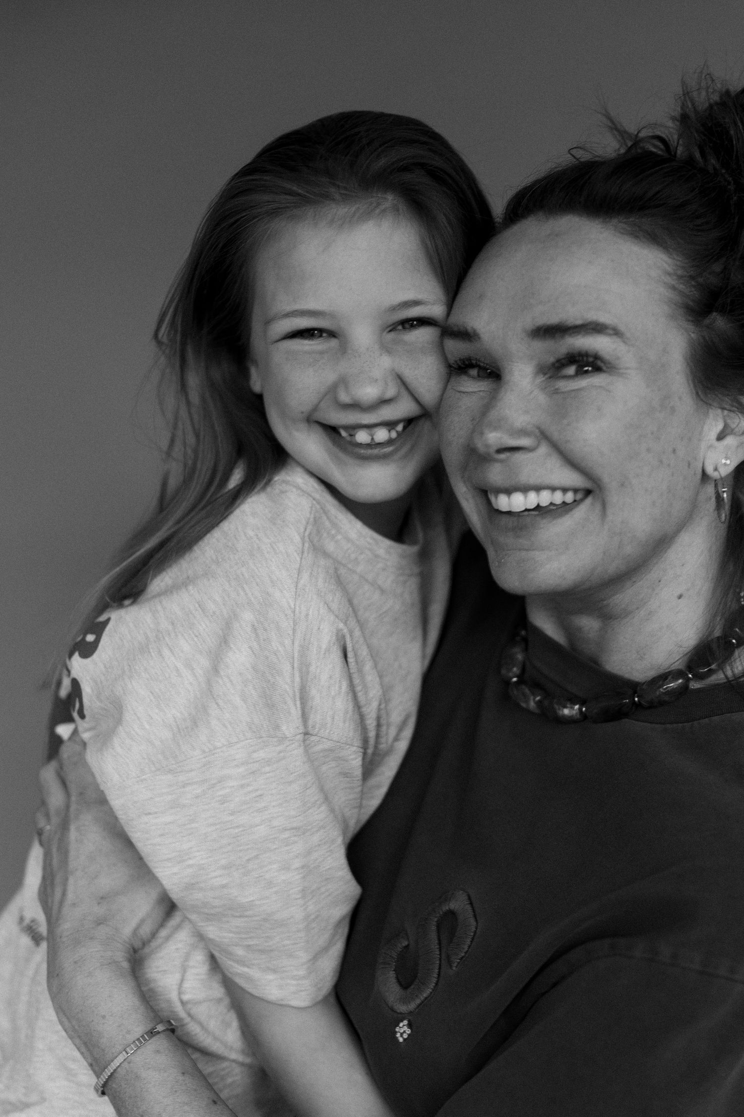 Black and white photo of a smiling woman and young girl cheek to cheek, sharing a joyful moment together.