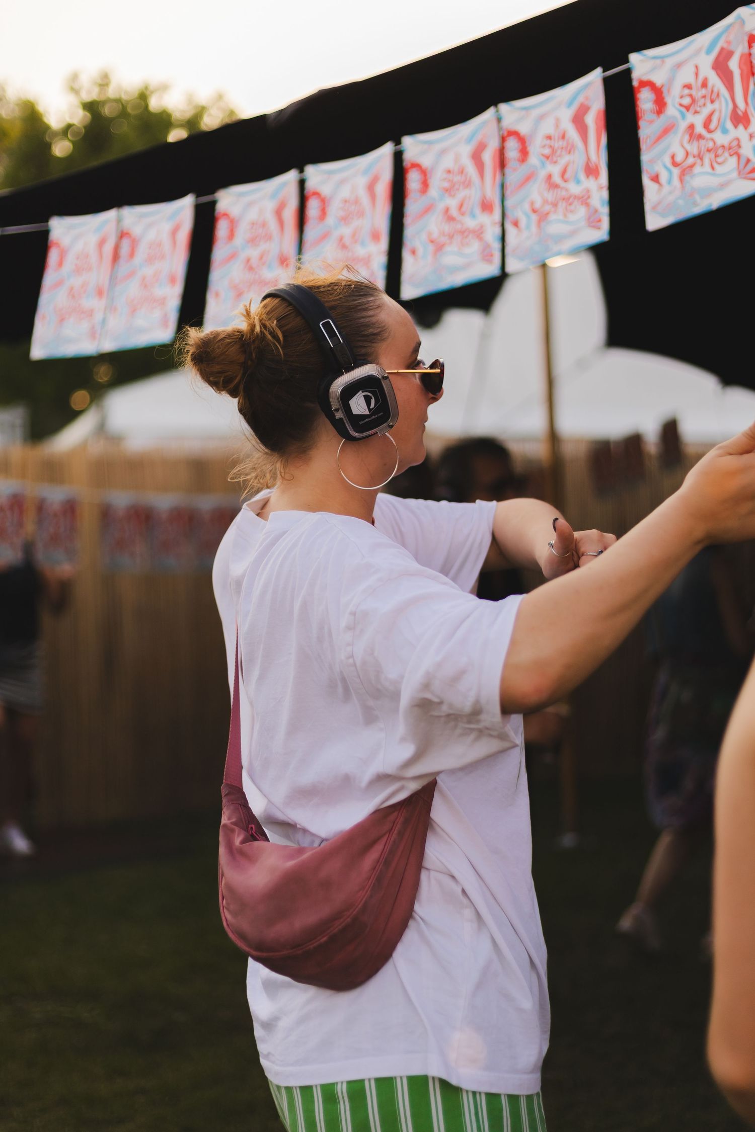 Person in white t-shirt dancing under decorative banners at an outdoor festival.