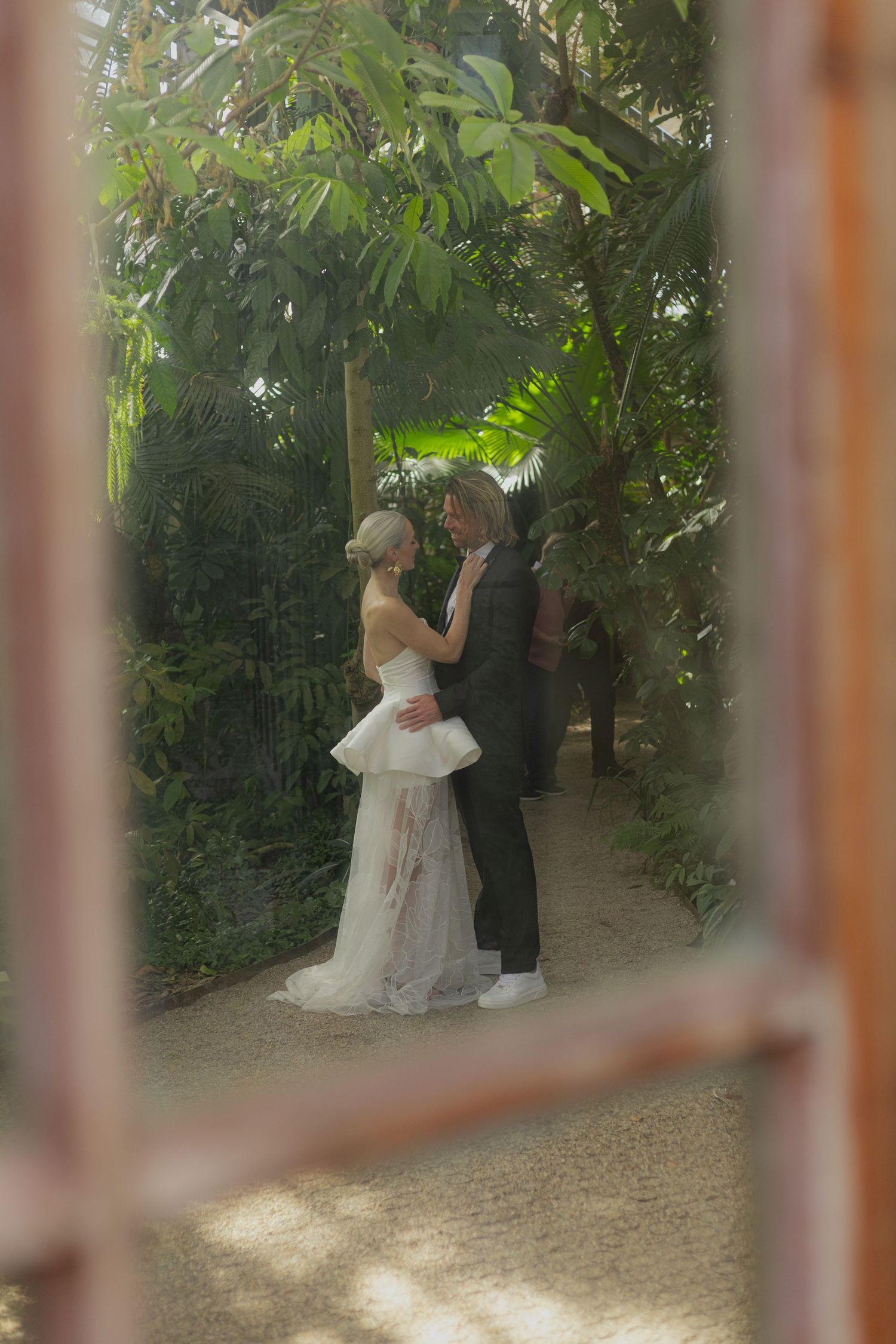 Wedding scene captured through window frames in a garden setting.