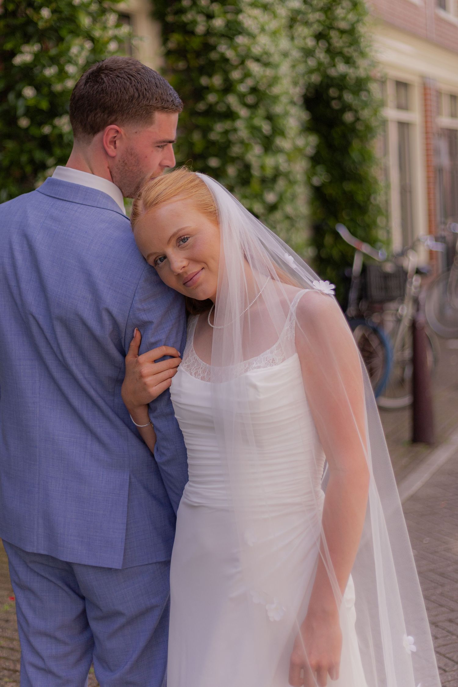 A bride in a white gown and groom in blue suit share an intimate moment outdoors.