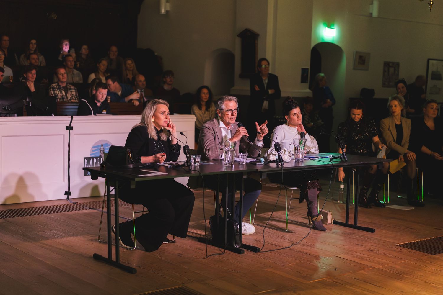 People seated in a dimly lit performance space with green lighting visible in the background.
