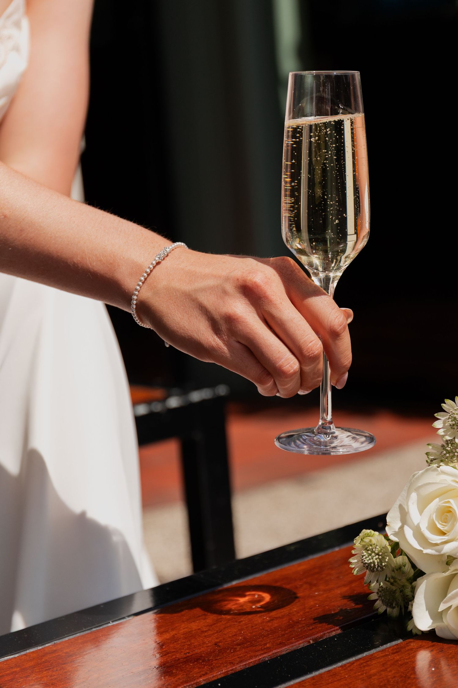 Elegant champagne glass being held by someone in a white dress against a dark background.