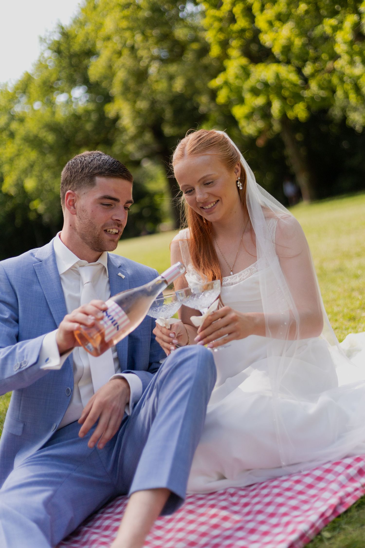 A couple enjoys drinks together on a red checkered blanket during their wedding celebration.