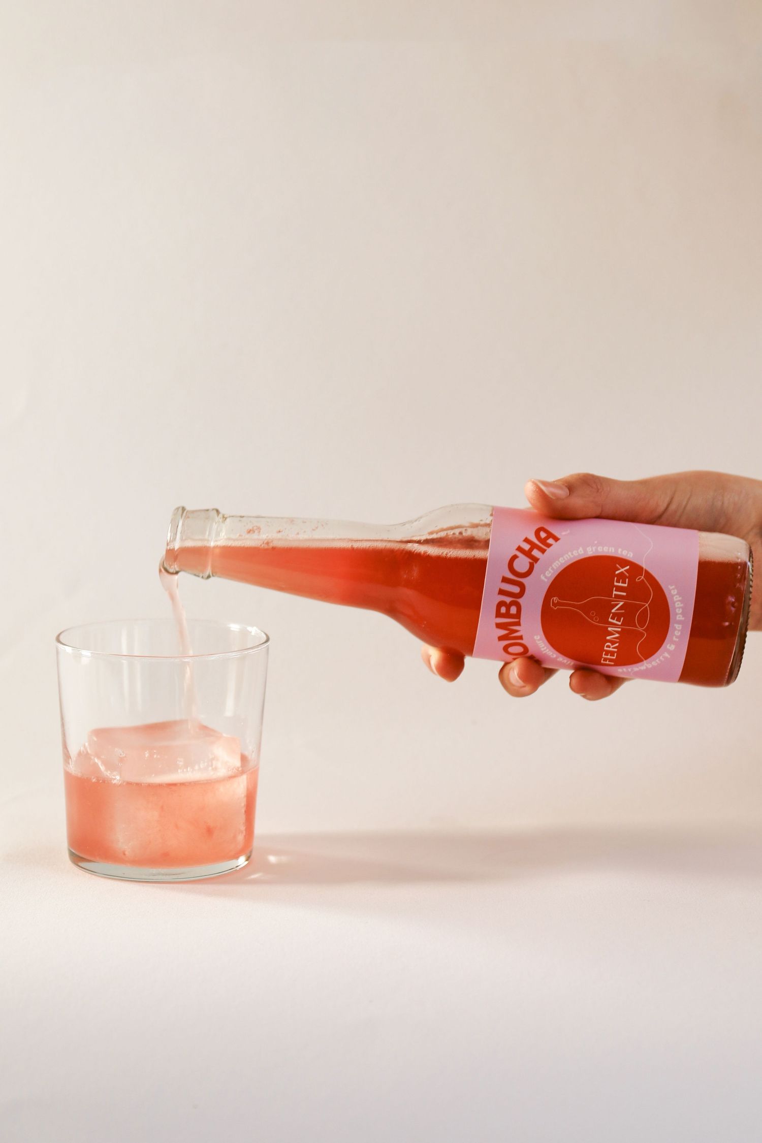 A pink beverage being poured into a clear glass on a white surface.