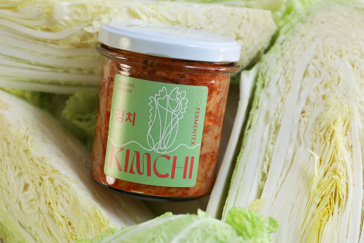 Fresh cabbage leaves and jars of kimchi arranged on a light surface.