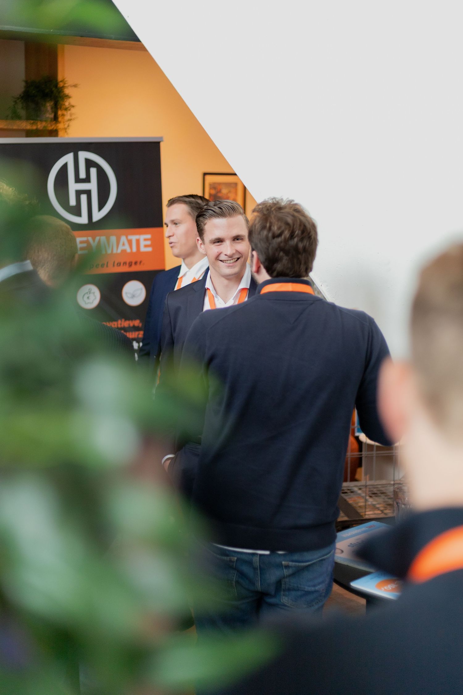 People networking at a business event with orange wall and company logo in background.