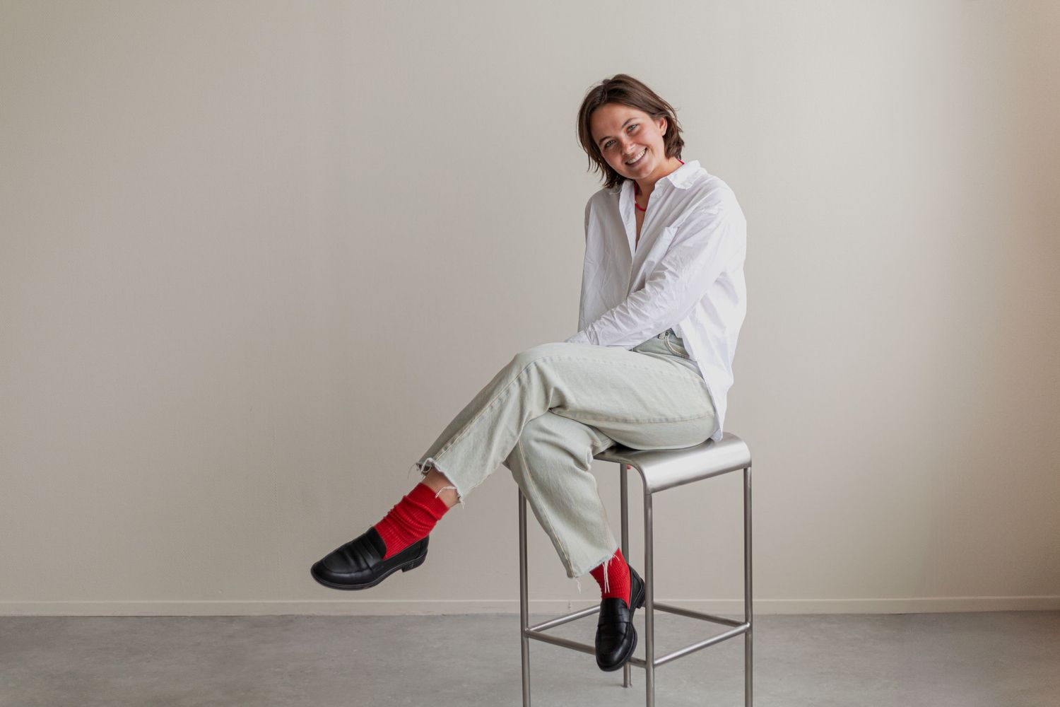 Person in white shirt and light pants sitting on metal stool wearing red socks.