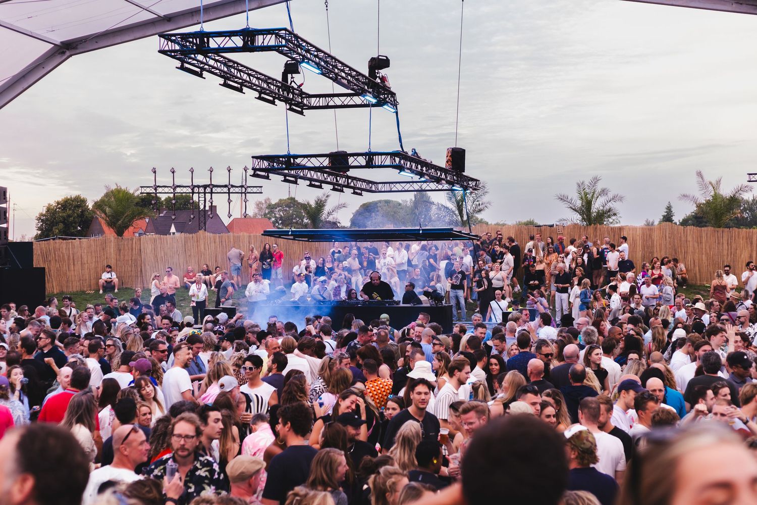 Large crowd gathered under outdoor festival tent during daytime event.