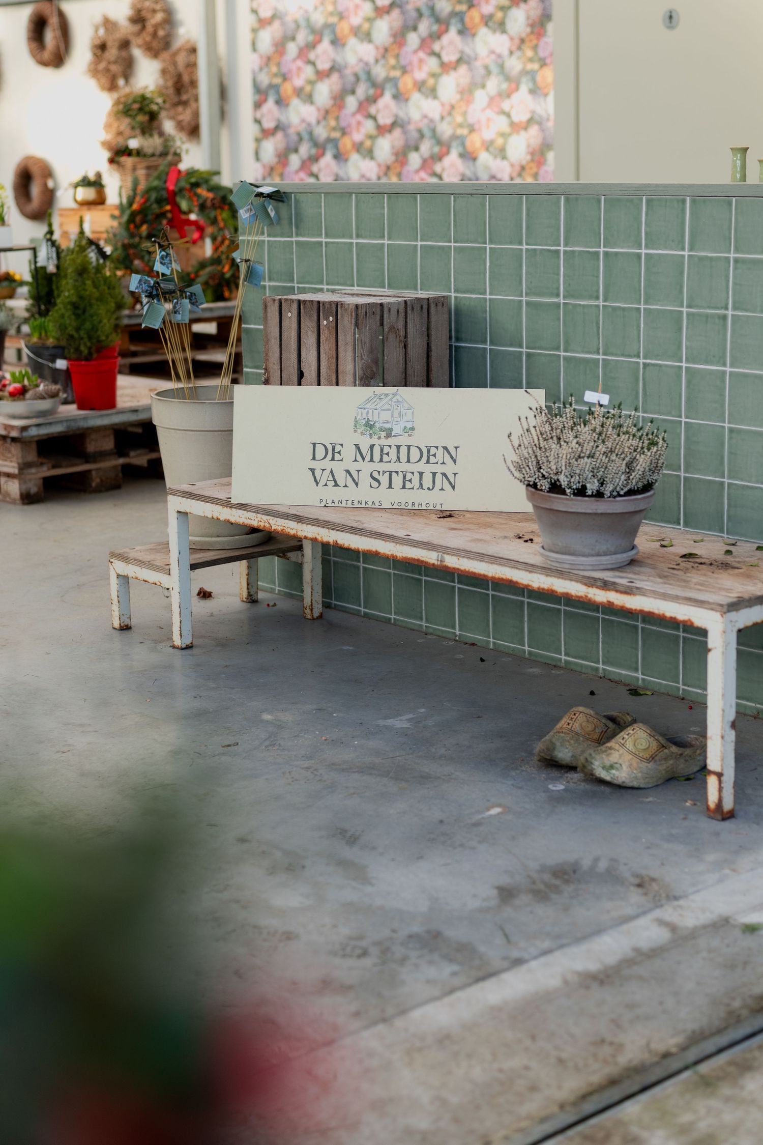 Vintage wooden bench with decorative pots sits against a tiled wall with floral wallpaper in a rustic interior setting.