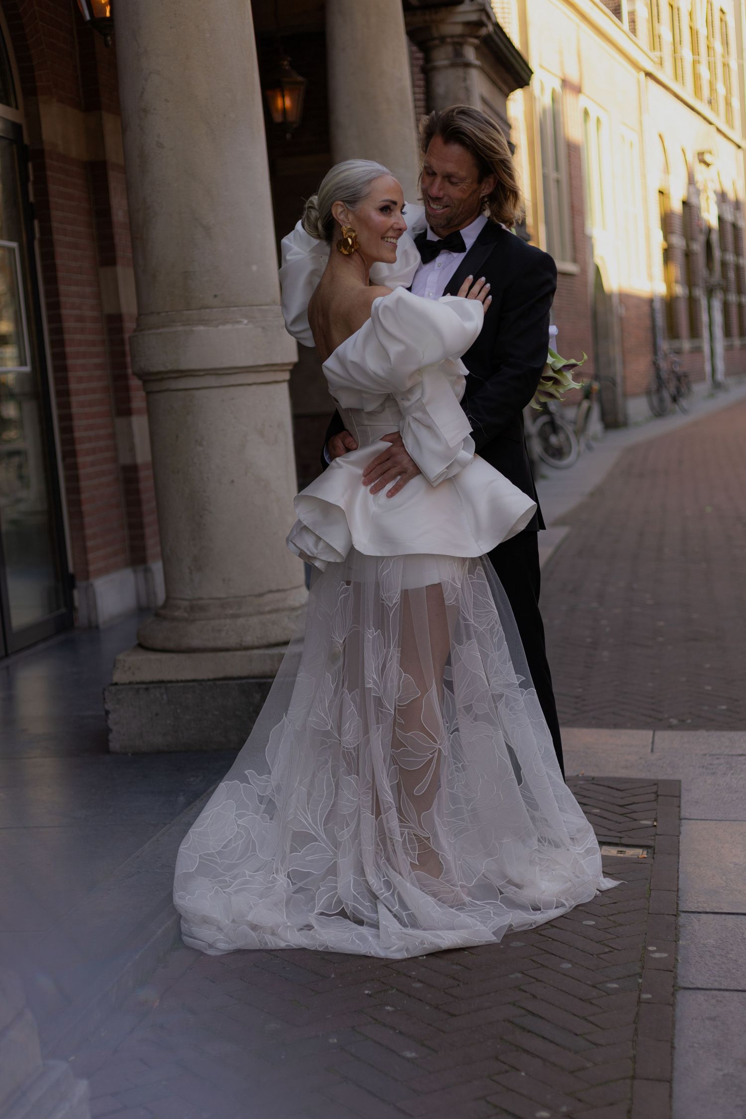 Newlyweds share an intimate dance moment along a colonnade with brick architecture.