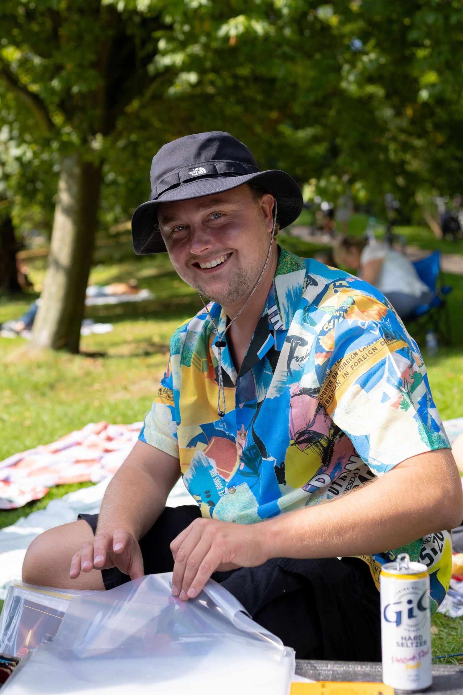 Person in Hawaiian shirt and cap relaxing at an outdoor event.