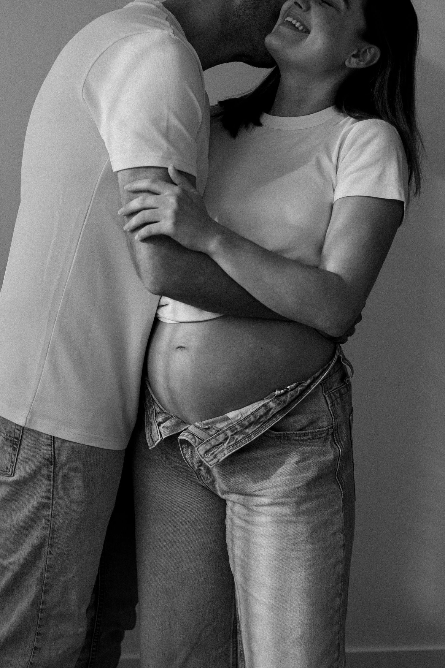 Black and white series showing romantic embrace between couple in jeans and white shirts against neutral background.