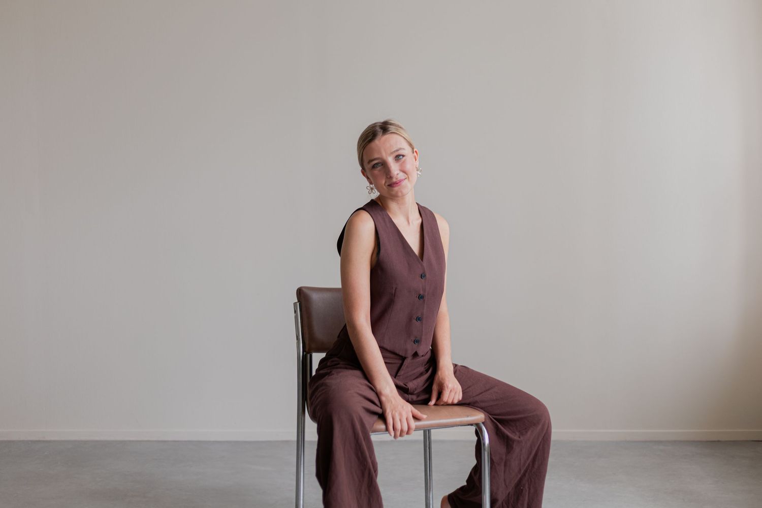 A person in a burgundy sleeveless jumpsuit poses in different positions against a white wall.