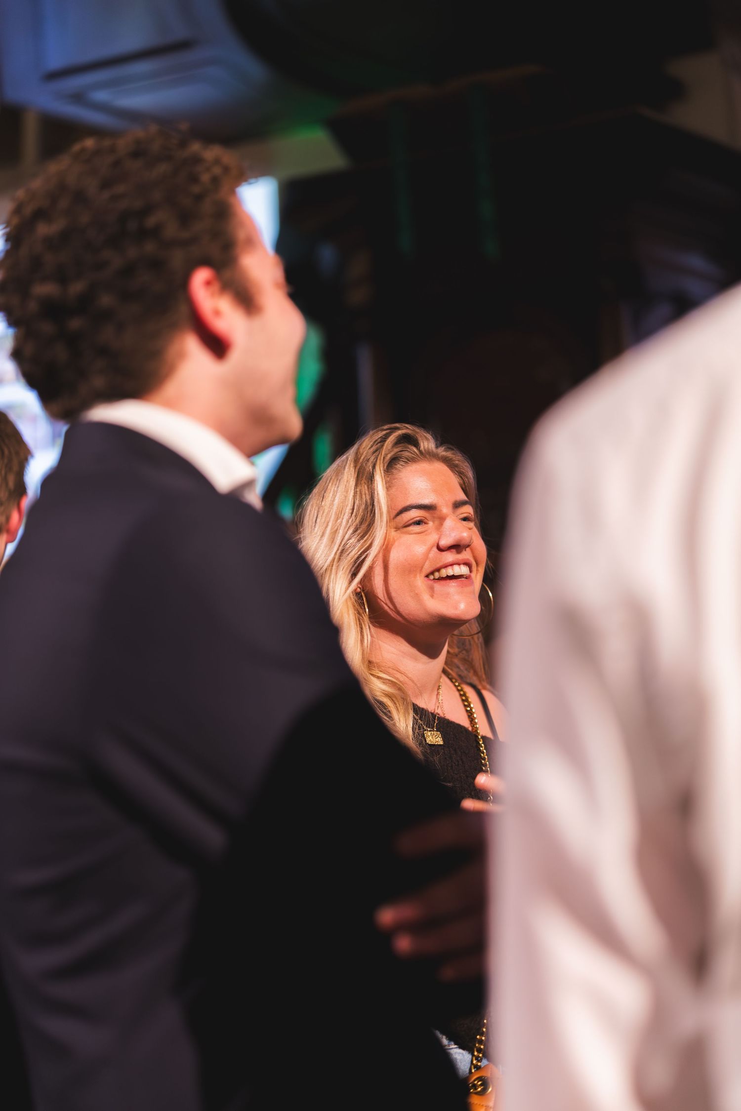 People share joyful laughter at a formal evening event in dark attire with dramatic lighting.