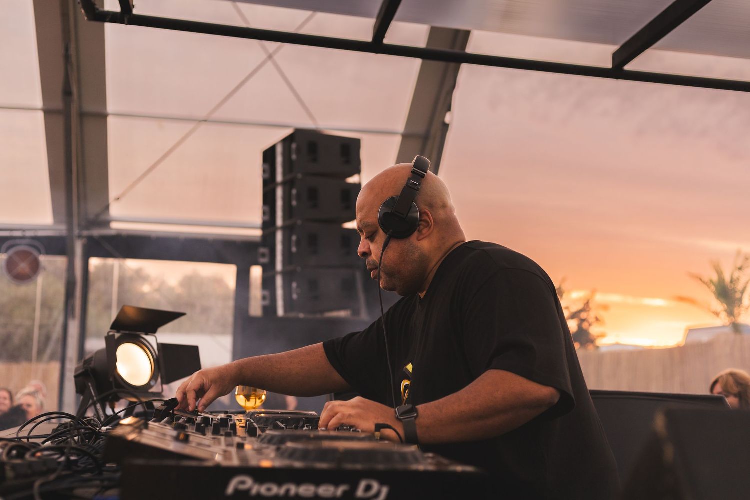 DJ performing at sunset under a large tent structure.