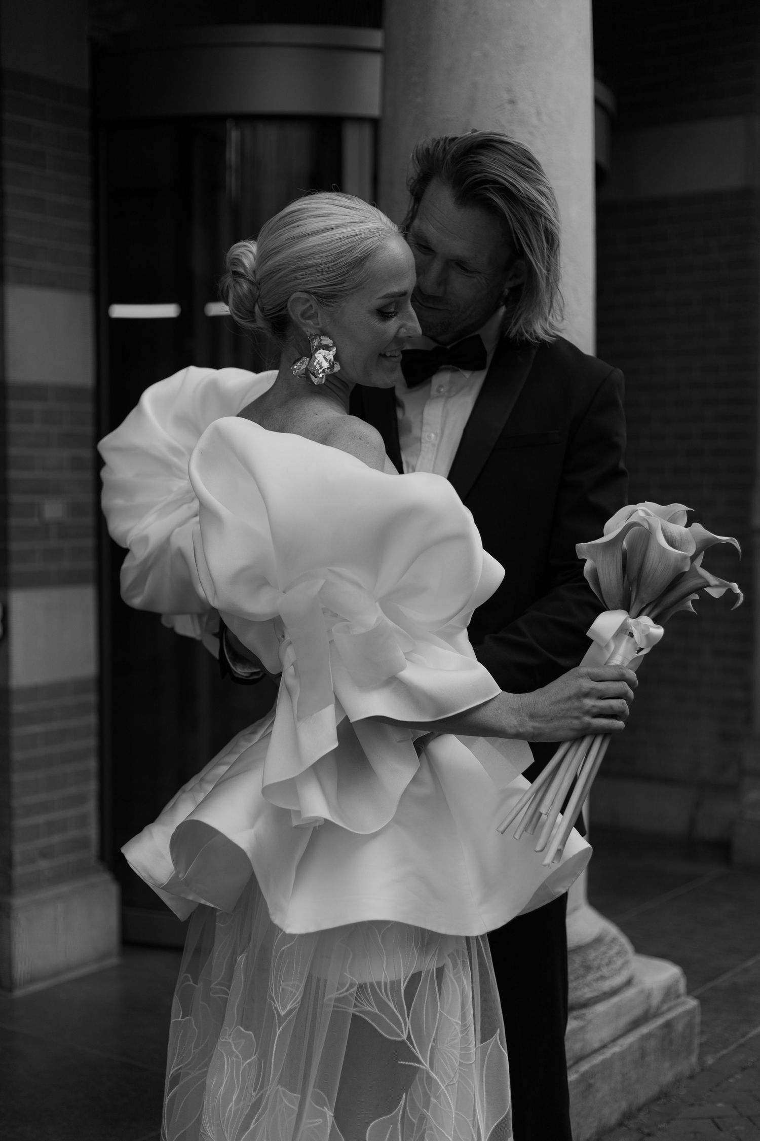 Dramatic black and white photo of a wedding dress with sculptural ruffles near columns.