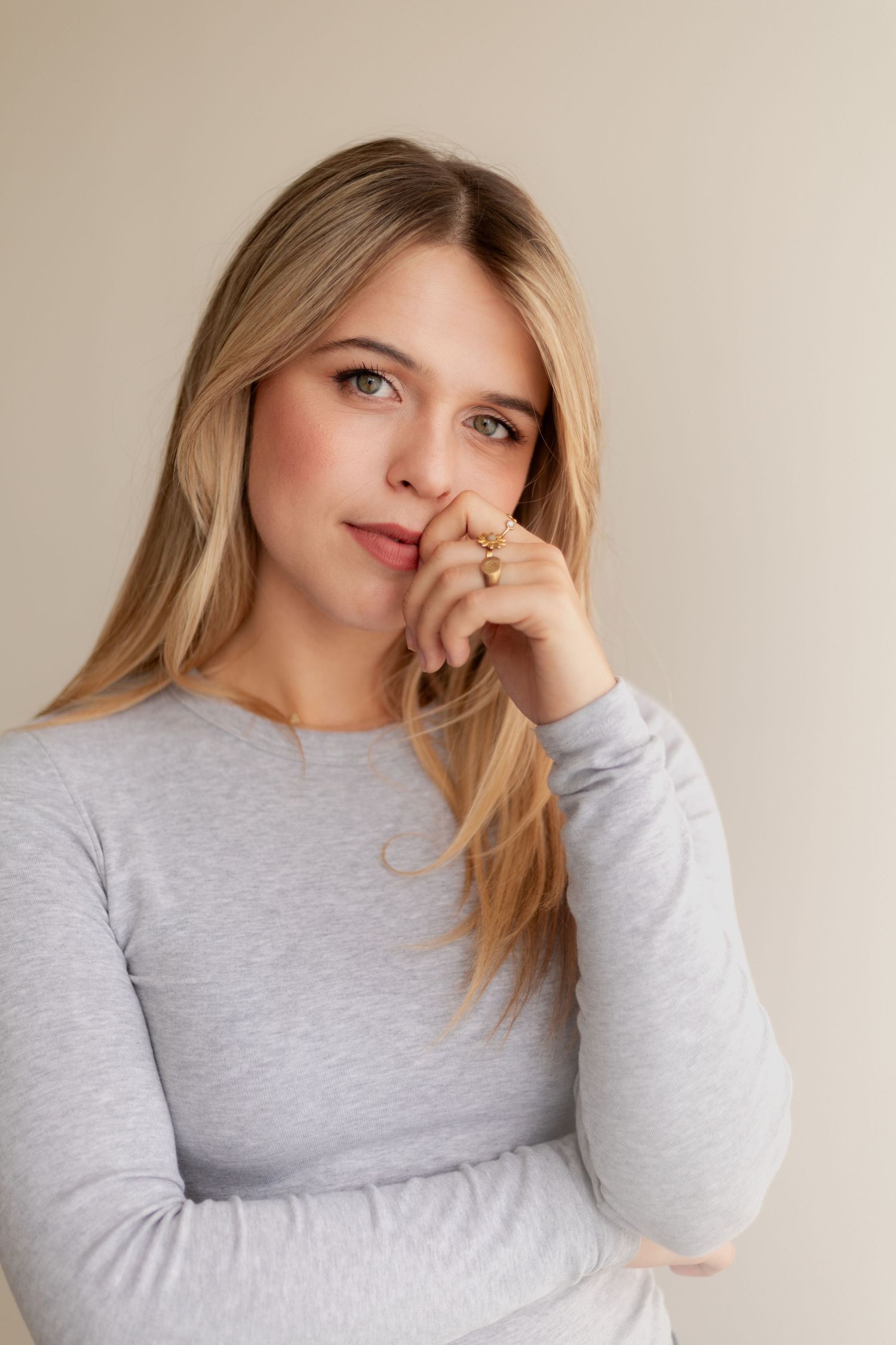 Person in a light gray sweater poses thoughtfully against a neutral background in a minimalist portrait series.