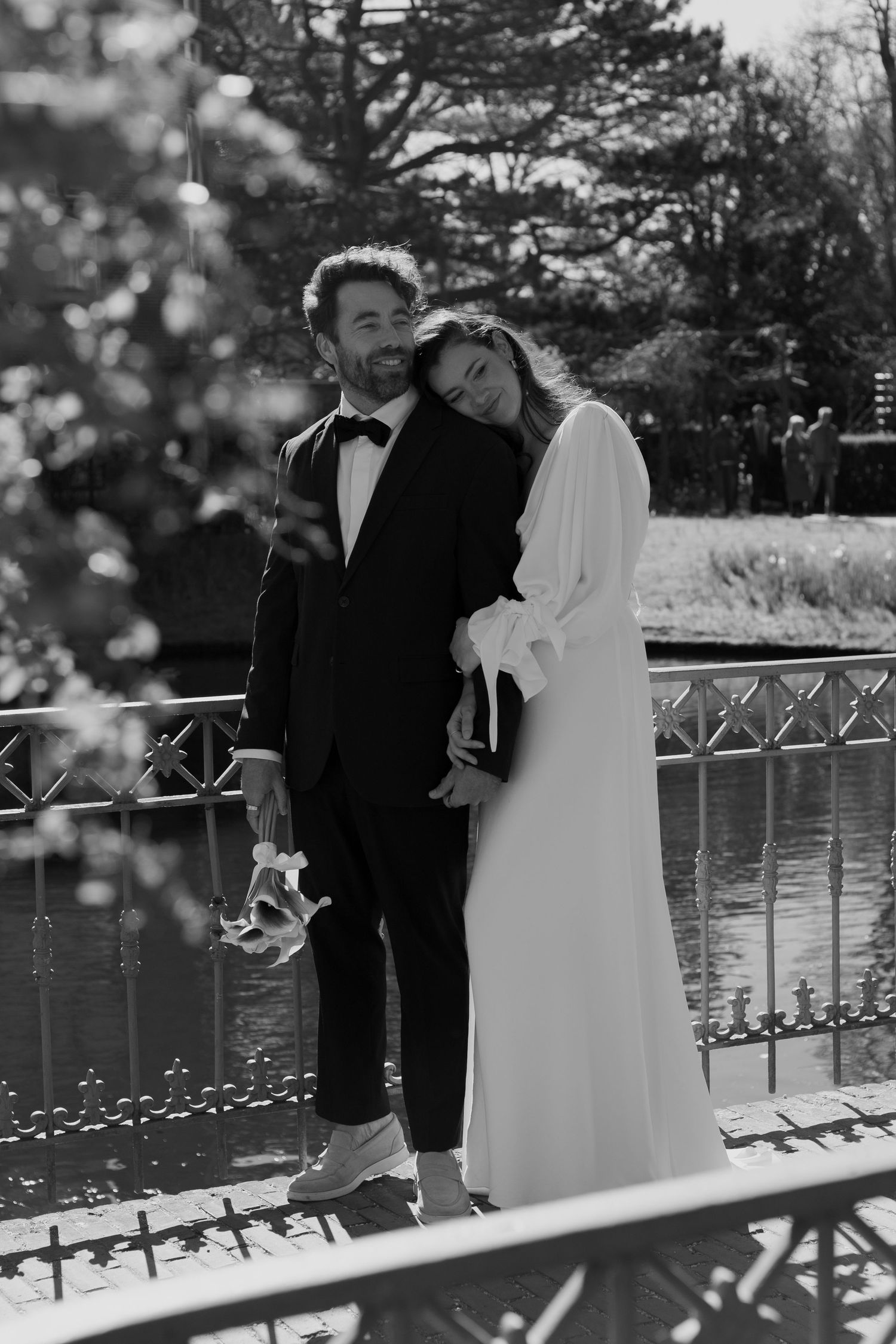 Romantic wedding couple embracing by a lake with decorative railing.