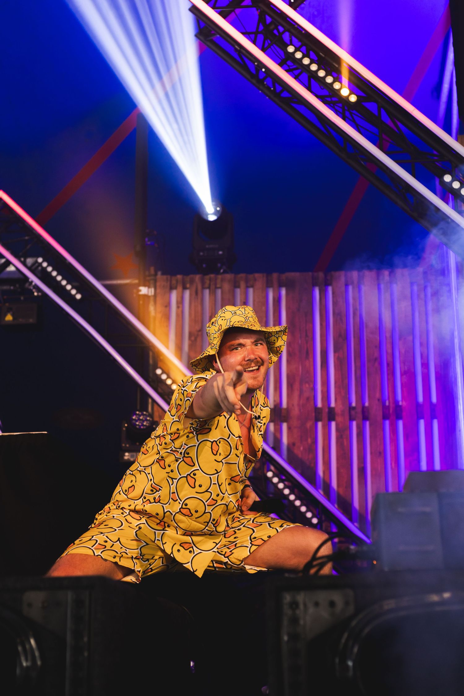 Performer in vibrant yellow patterned outfit lying down on stage with dramatic purple and blue lighting effects.