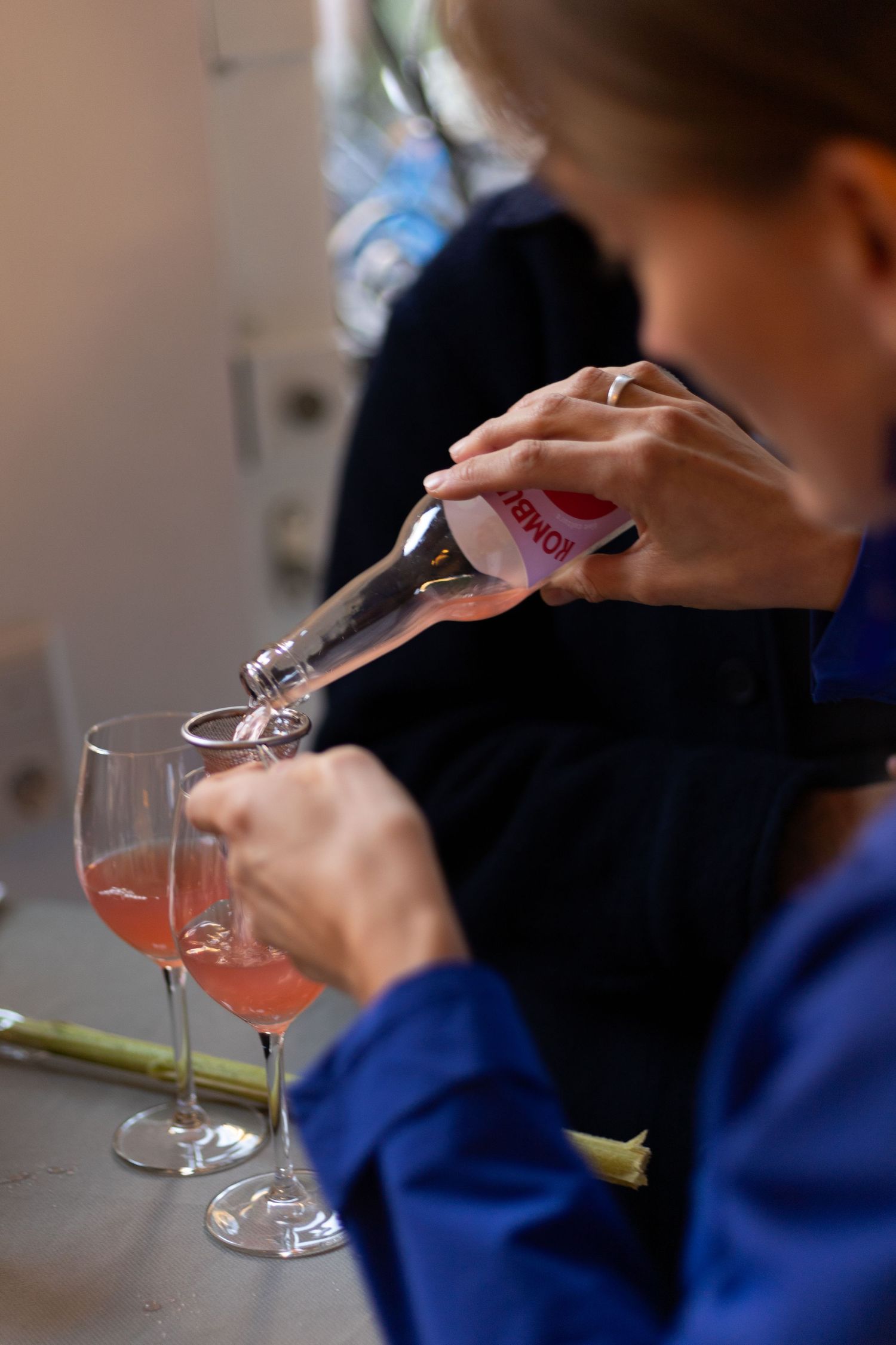 Someone pours a pink cocktail into stemmed glasses on a light colored surface.