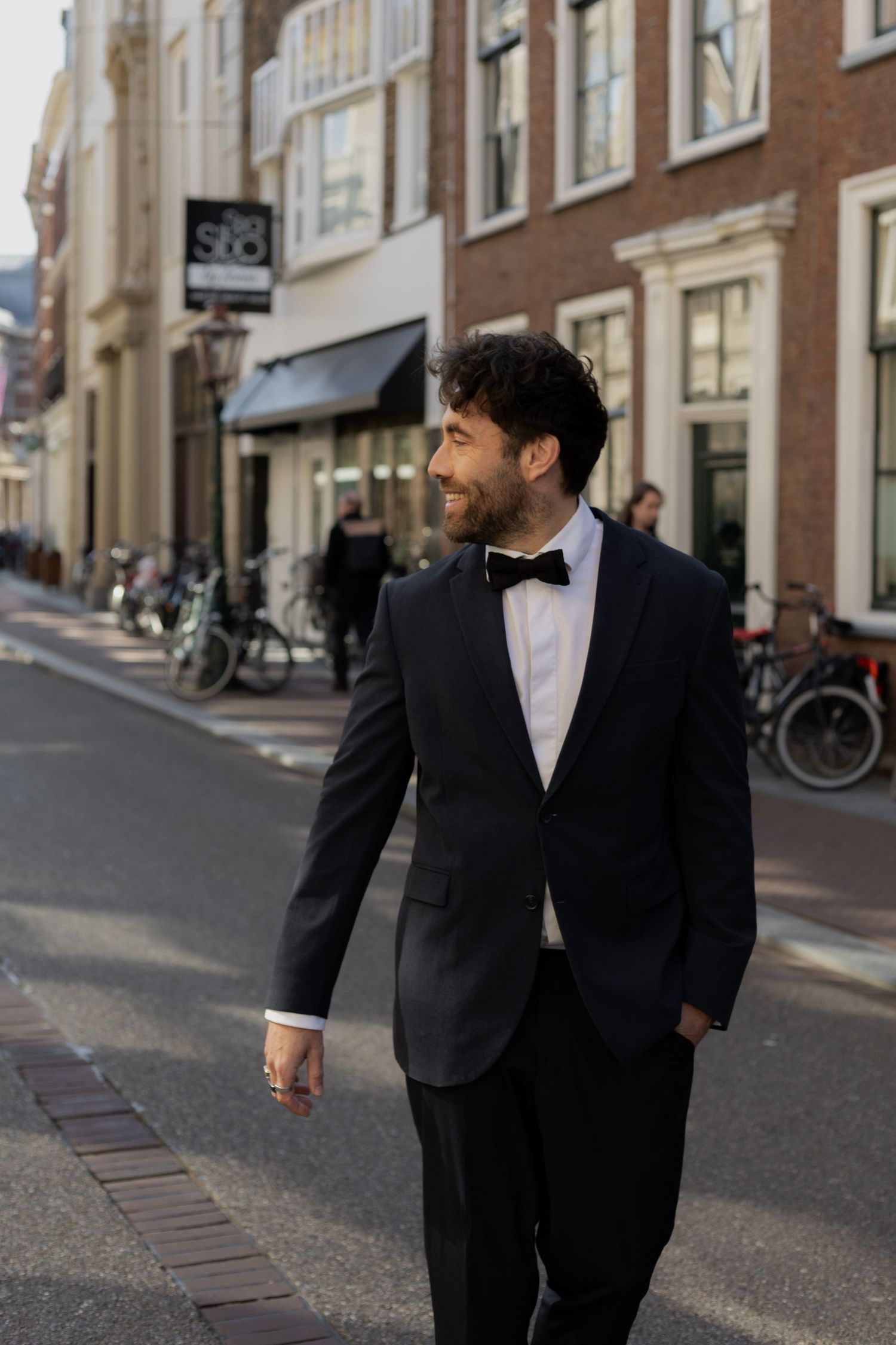 Two people in formal black attire walk down an urban street.