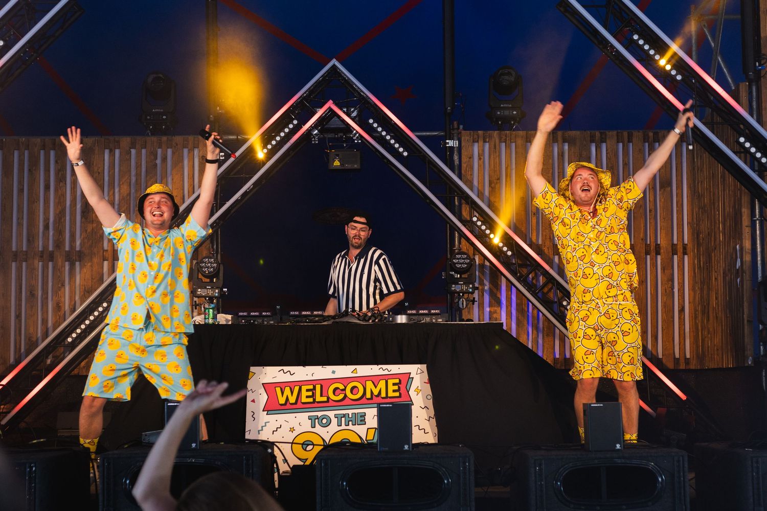 Wide shot of performers on stage with colorful lighting and wooden backdrop.