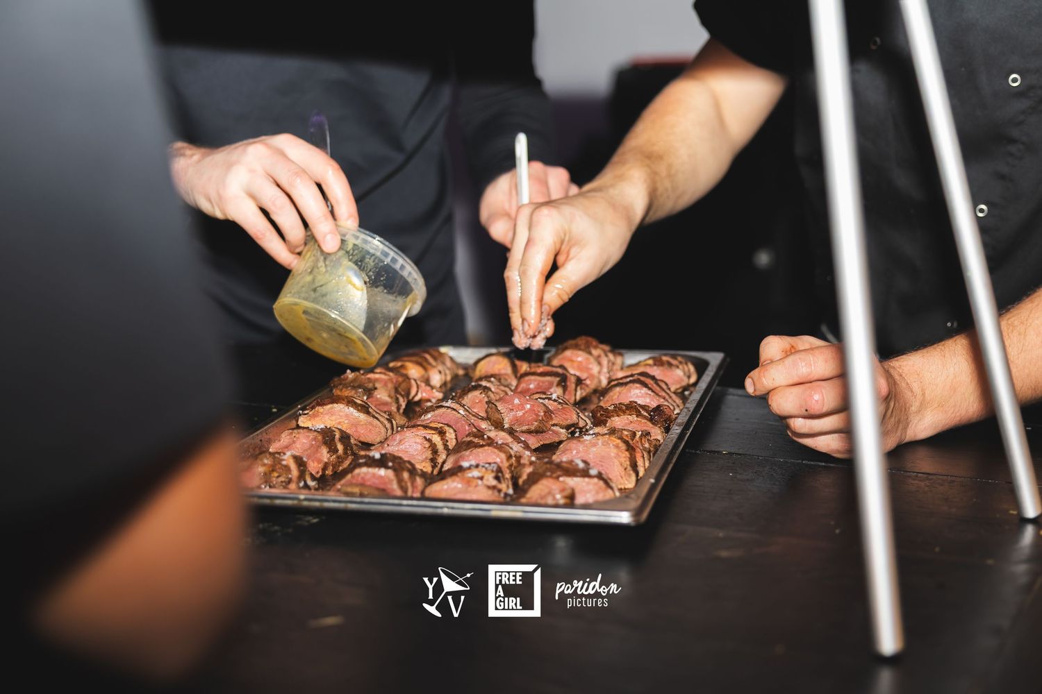 Hands preparing and seasoning raw meat on a dark cutting board in a restaurant kitchen setting.