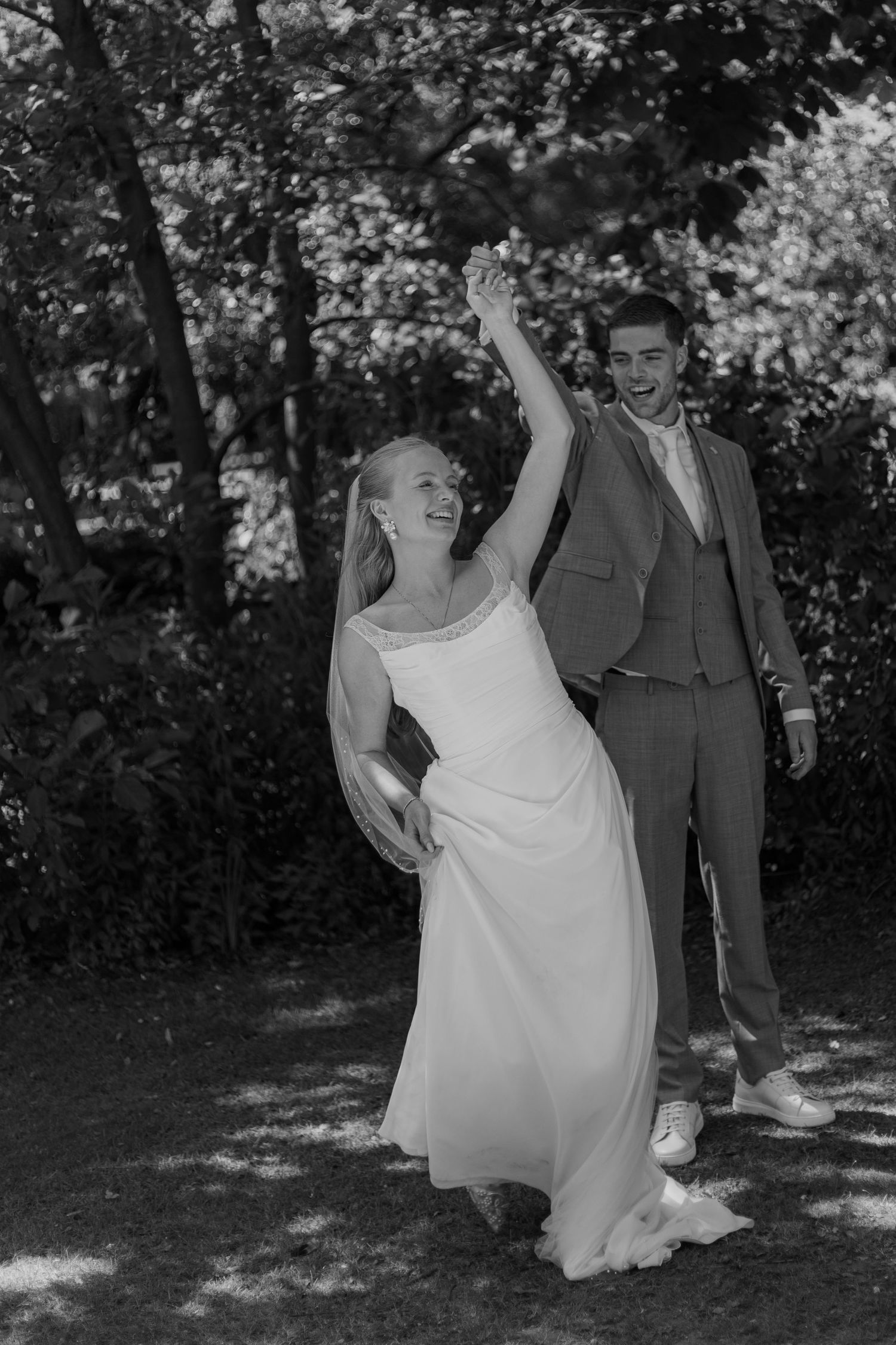 A wedding couple shares a fun dance moment in a shaded garden setting.