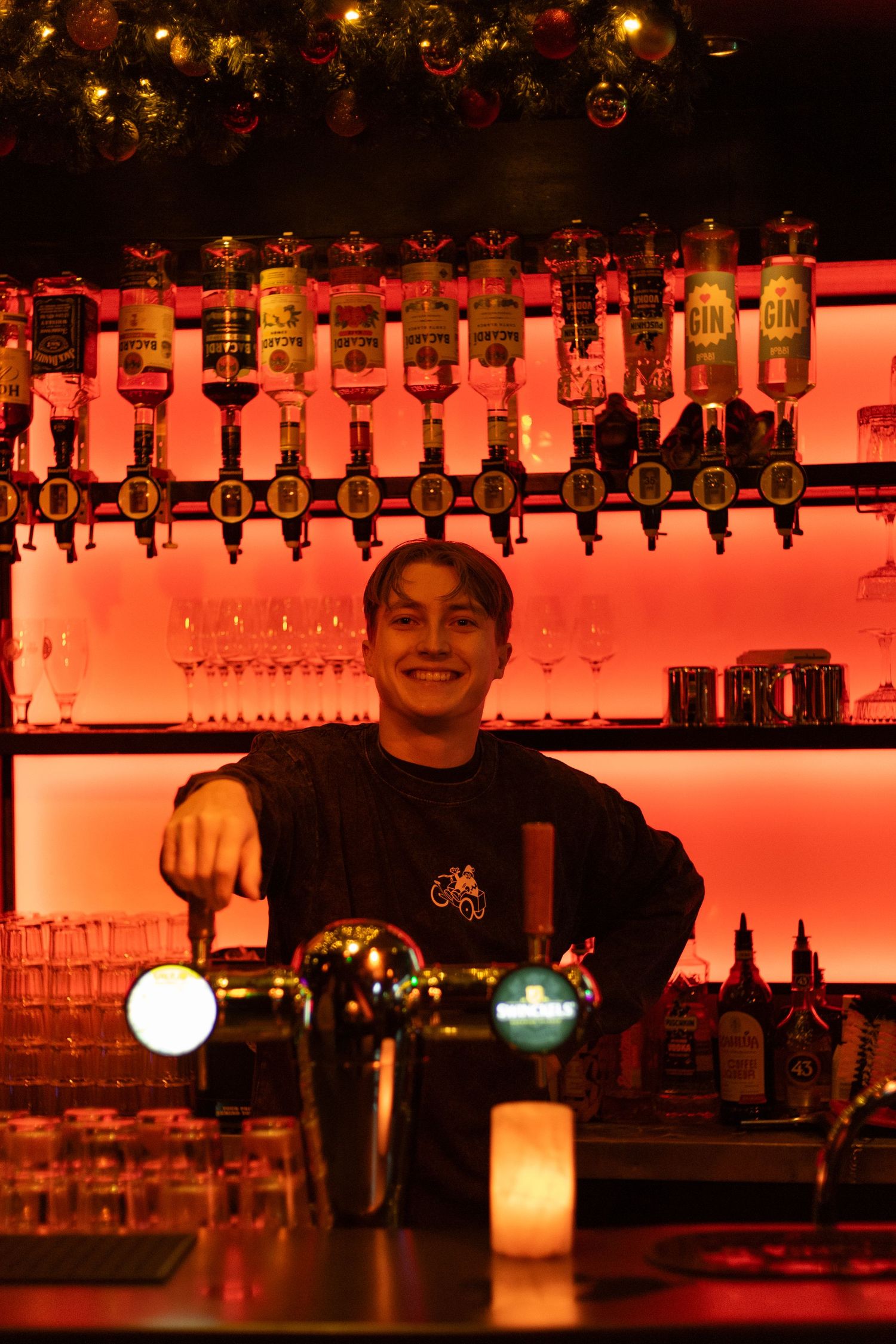 Bar interior with illuminated bottles on shelves casting warm red lighting.