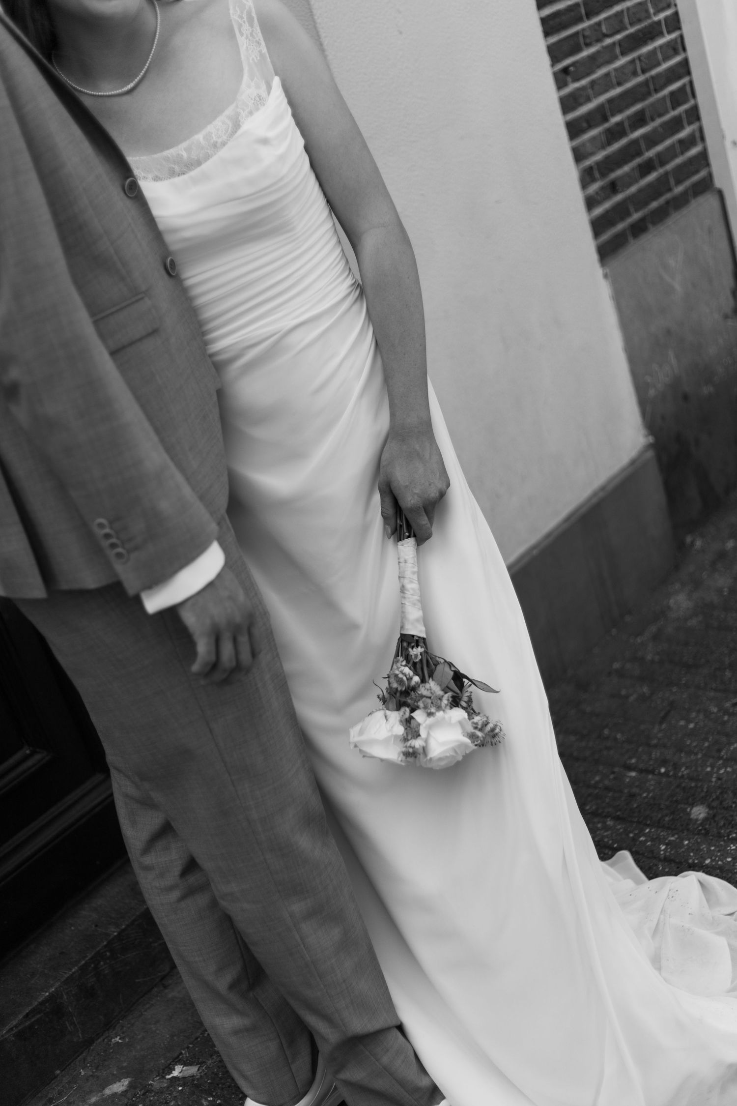 Black and white wedding photo showing the elegant details of a bride's dress and groom's suit.