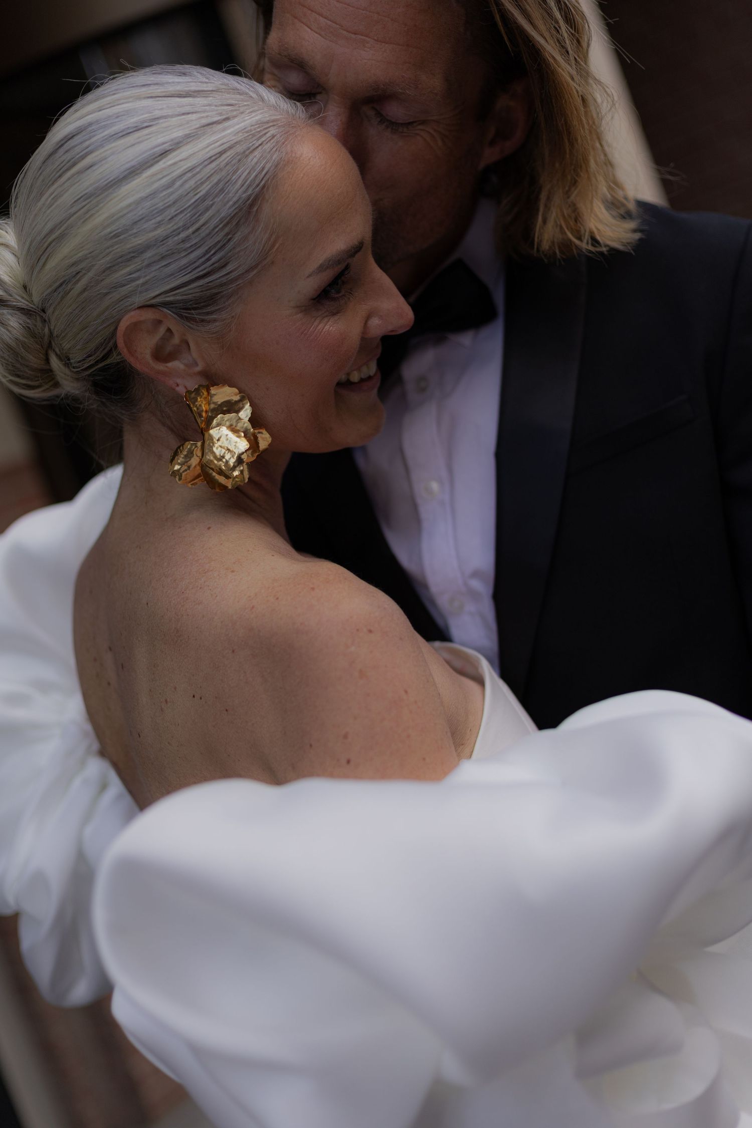A romantic wedding moment showing the elegance of a white dress with statement shoulders and gold earrings.