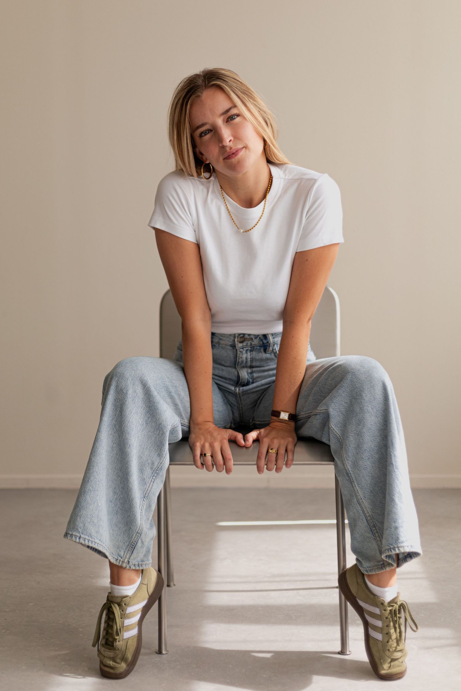 Person in white tee and light jeans sits casually on white bench wearing retro sneakers.