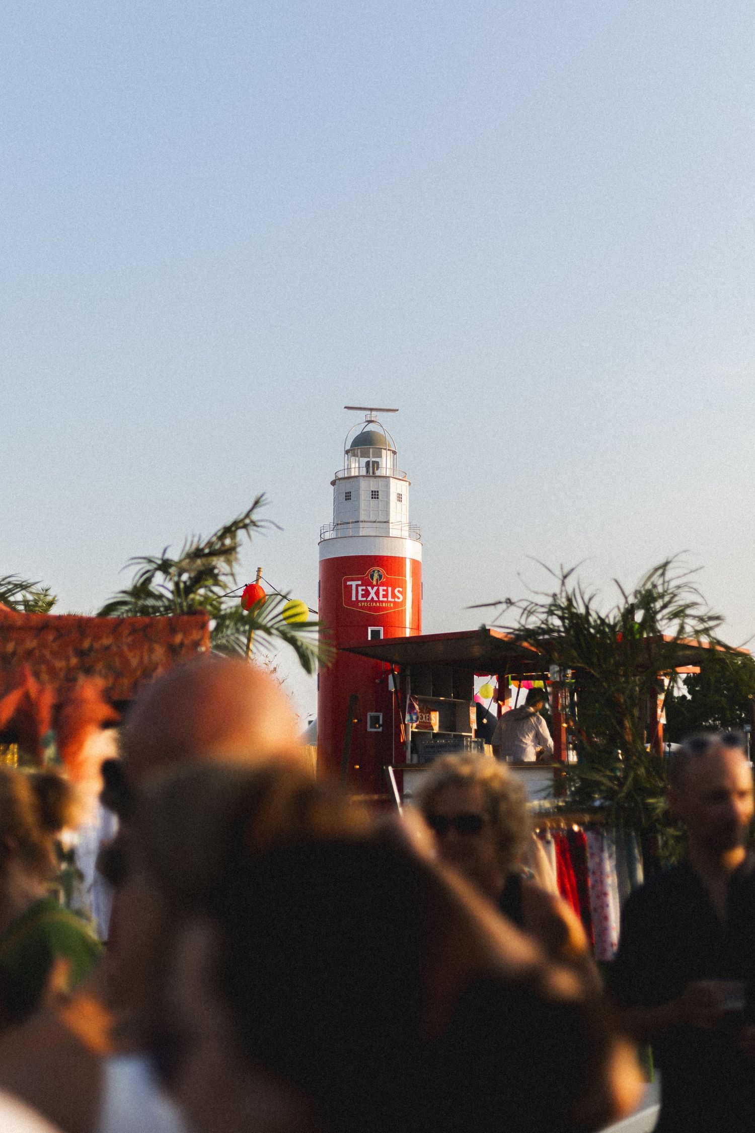 Red and white lighthouse tower silhouetted against a bright blue sky at sunset.