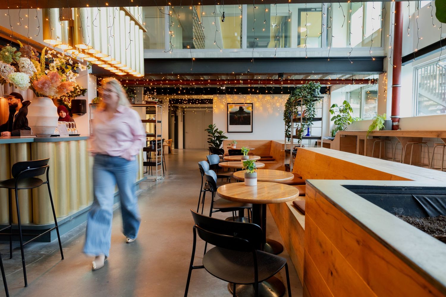 Modern cafe interior with wooden furniture, orange booth seating, and a customer walking through the bright dining space.