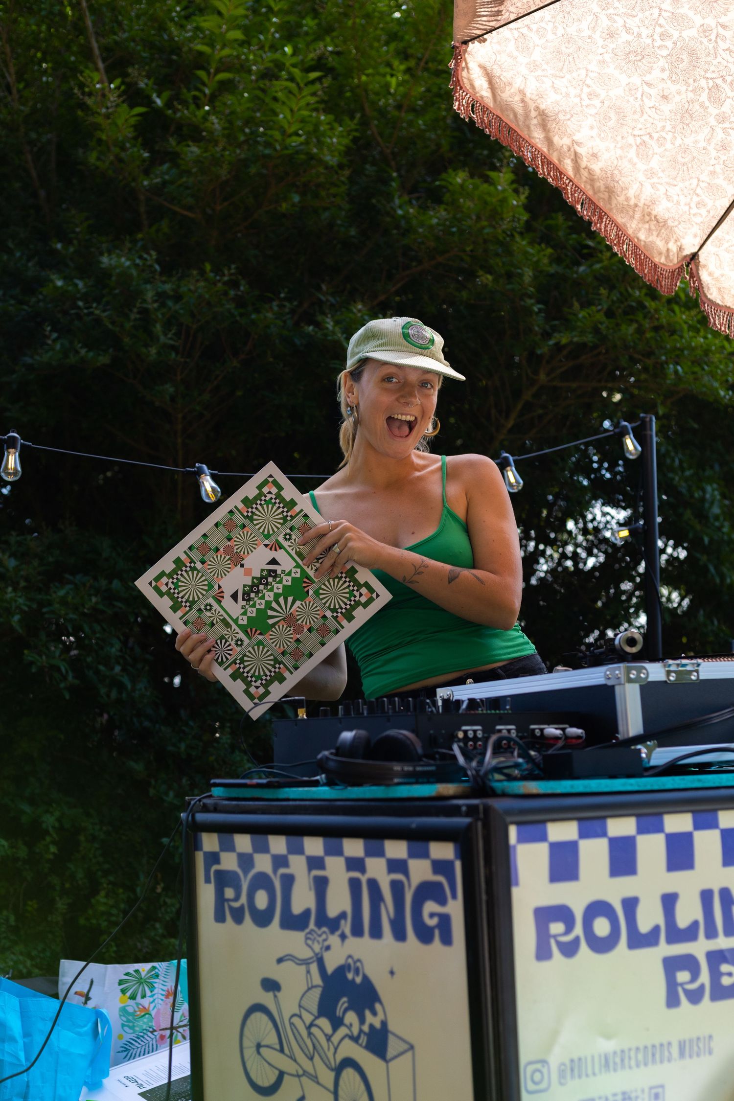 Person in green at a Rolling Records display booth sorting through vinyl records outdoors.