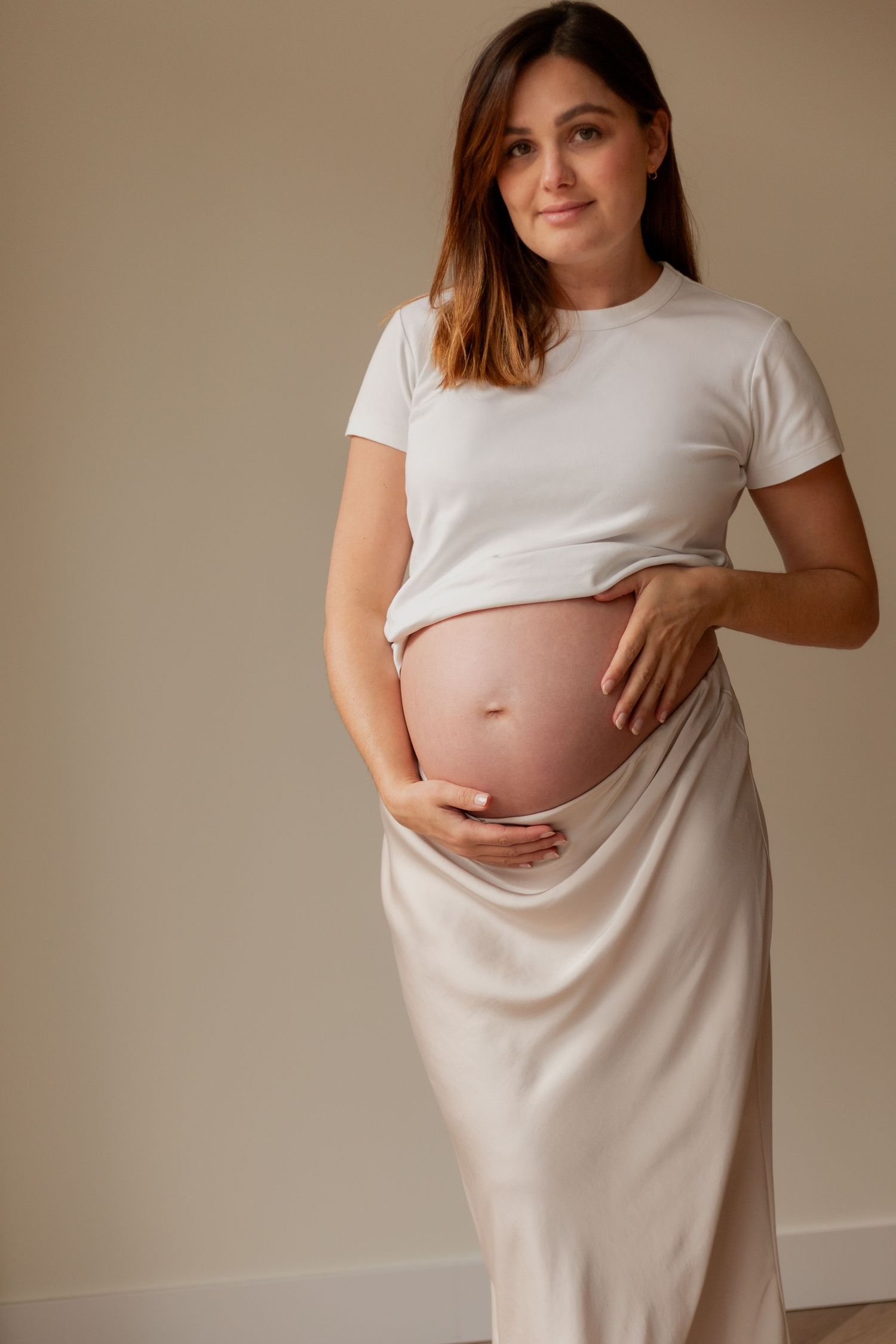 A sequence of maternity photos showing a pregnant woman in white against a neutral backdrop touching her belly.