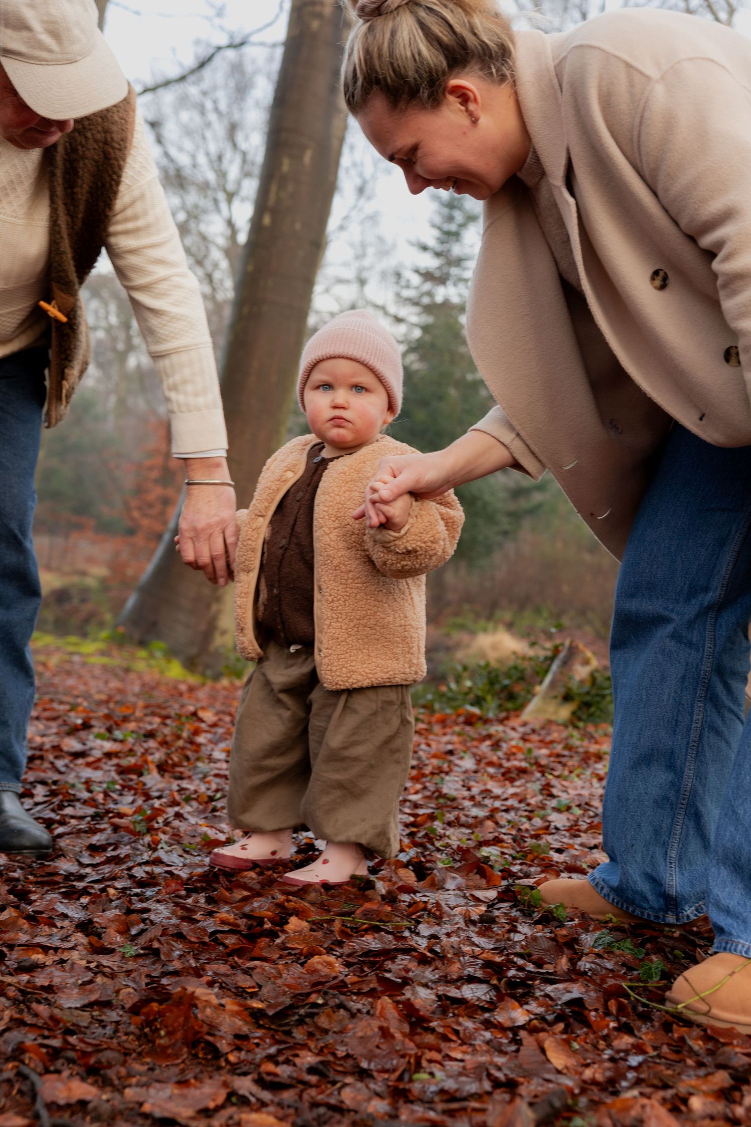 Small feet in brown shoes stand on a carpet of fallen autumn leaves in a forest setting.