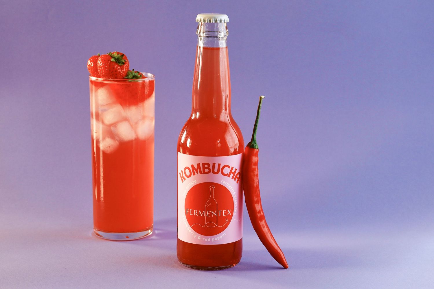Red kombucha beverages garnished with cherries in tall glasses against purple background.