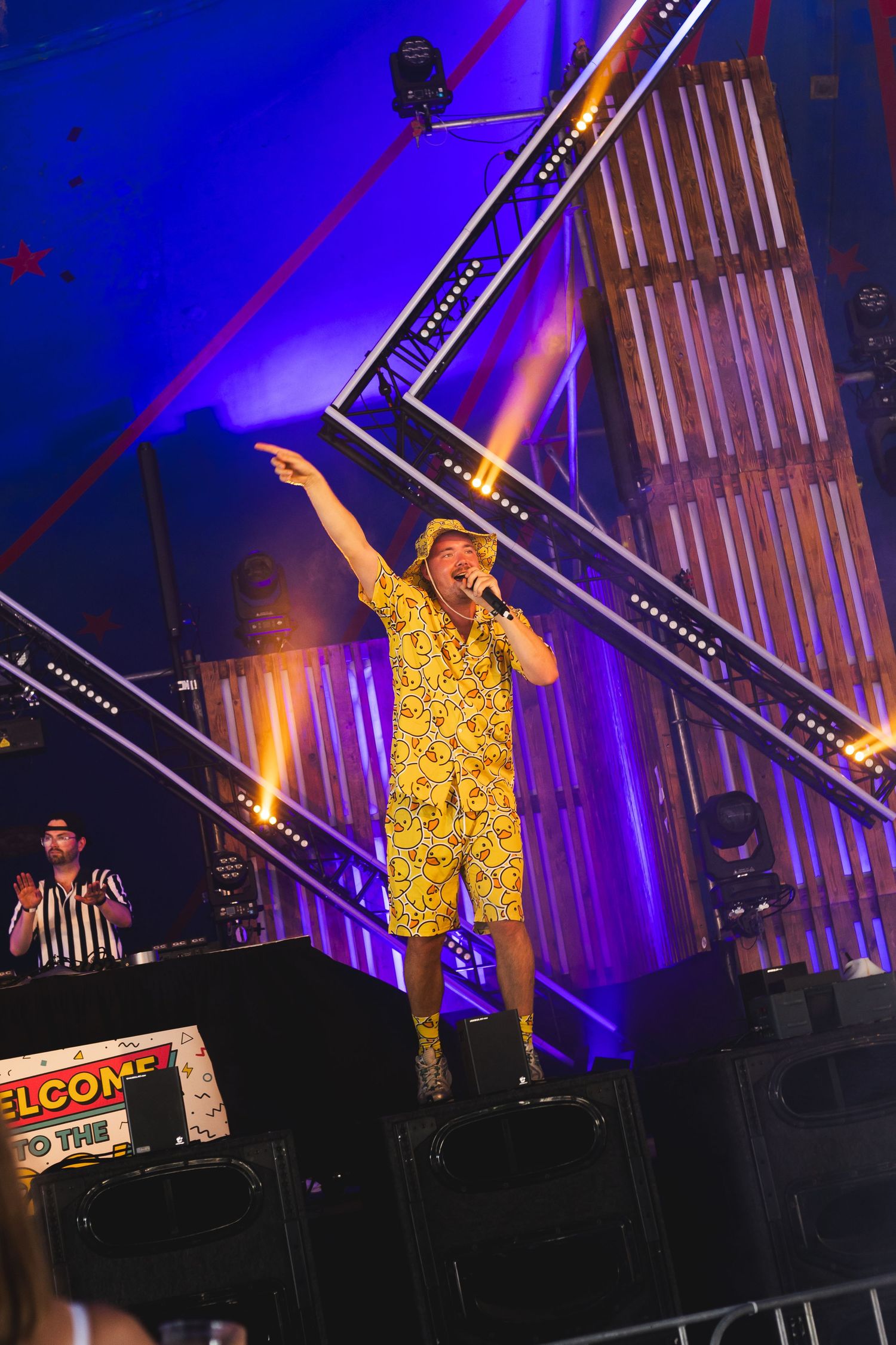 Performer in yellow patterned outfit dancing energetically on stage with dramatic purple lighting.